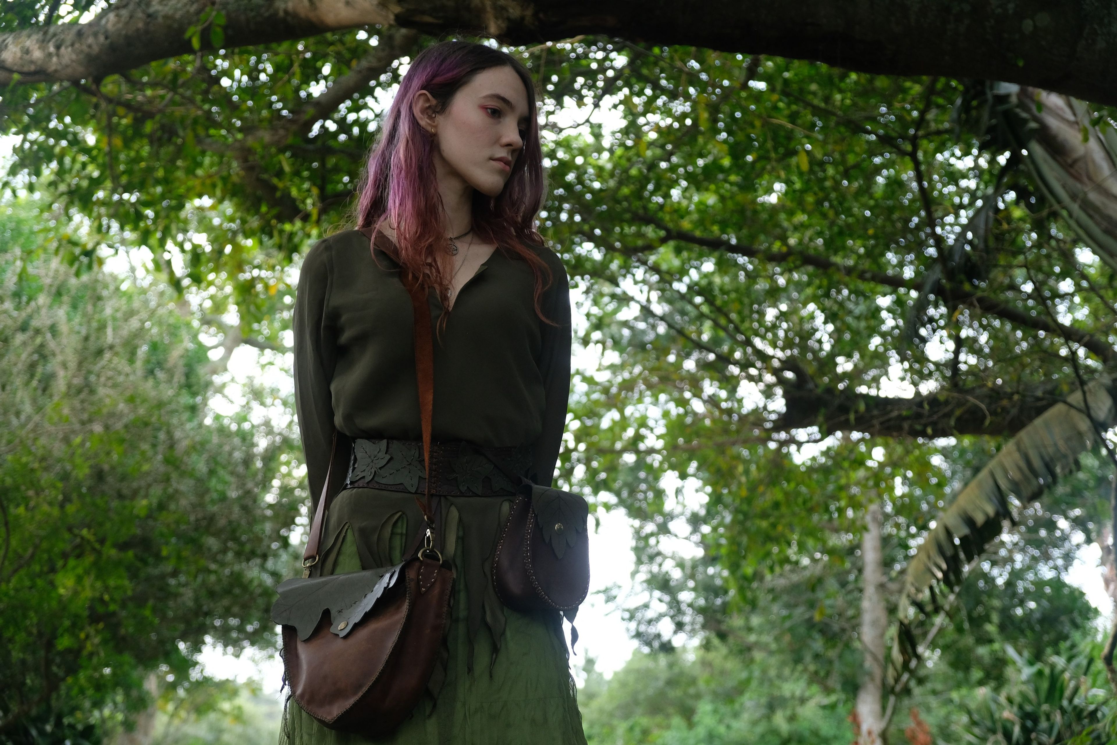 Woman standing under a tree with a leather bag at her hip