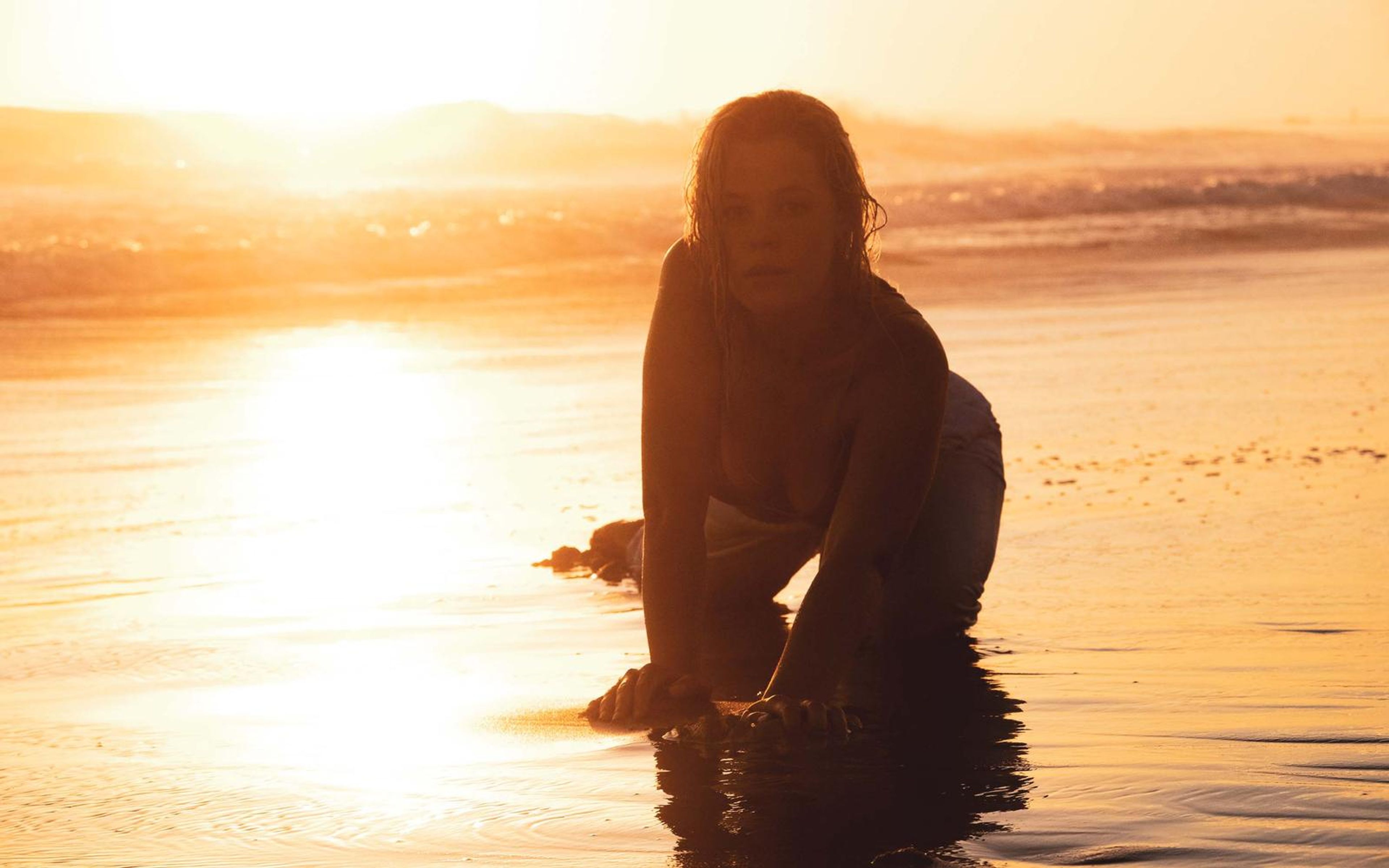 Woman kneeling on hands and knees in a golden pool of sunset light, silhouetted, reflection below