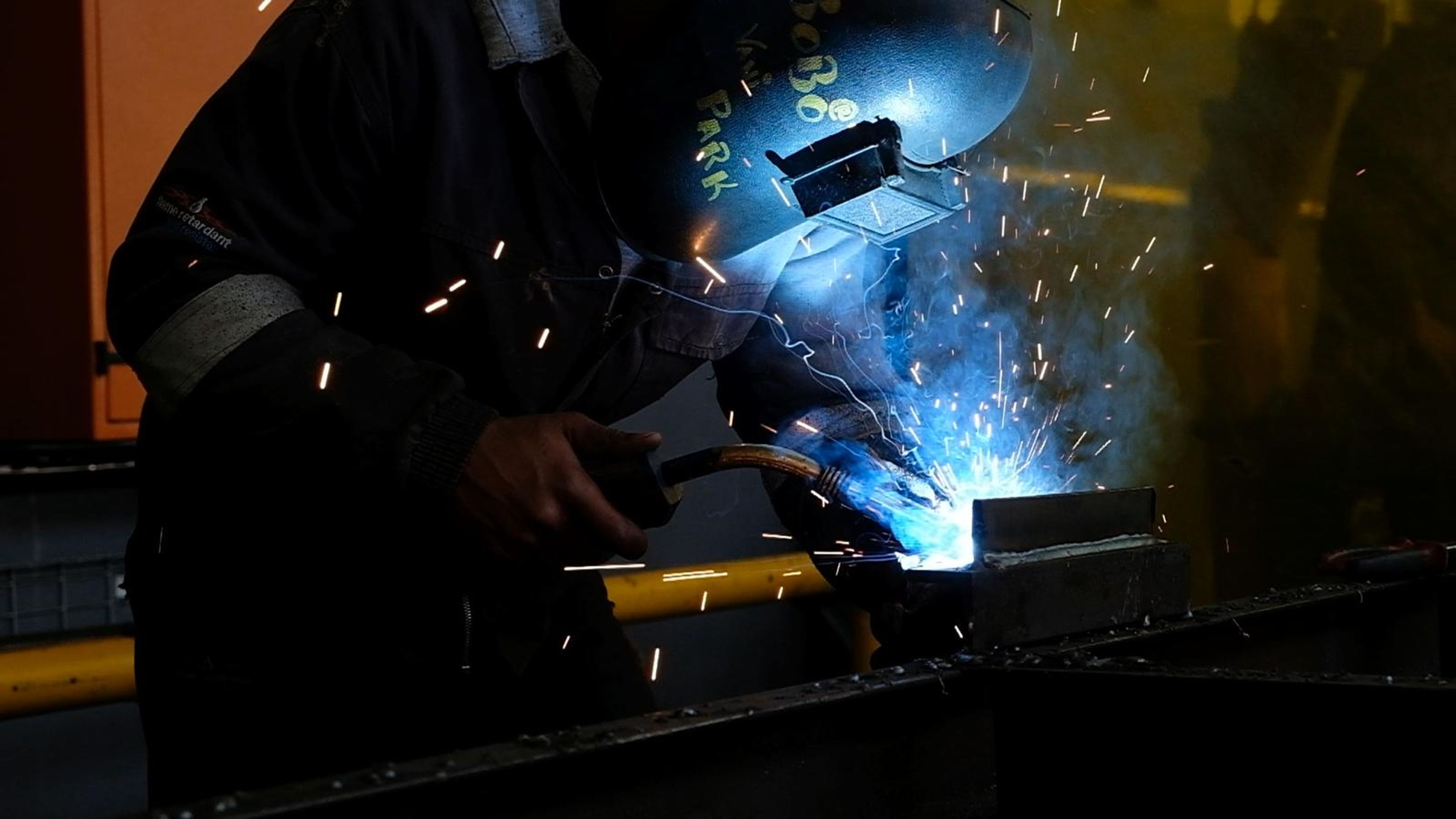 Welder in a helmet working at a steel section under a blue arc