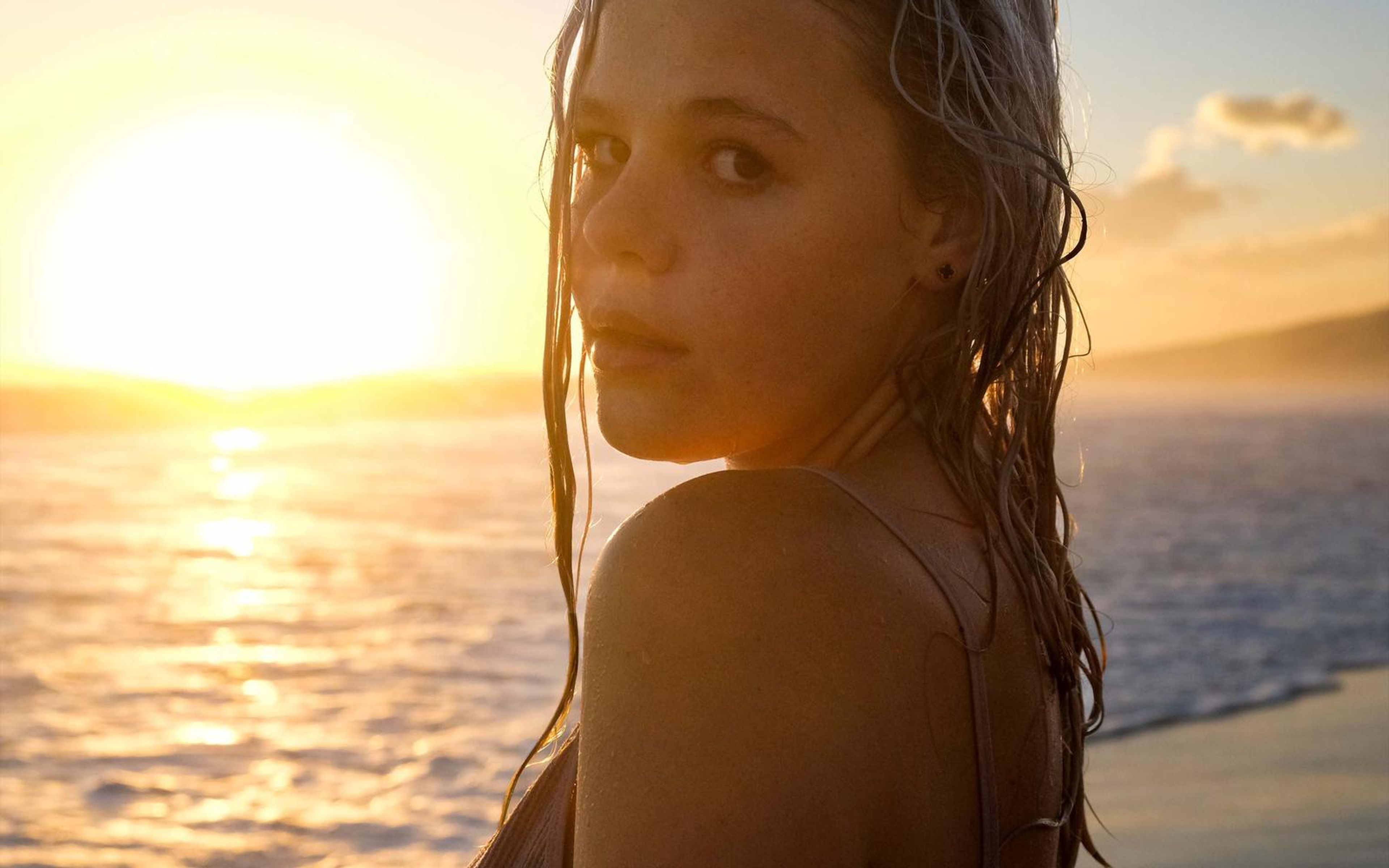 Woman glancing over her shoulder at the camera with wet hair, golden sea behind