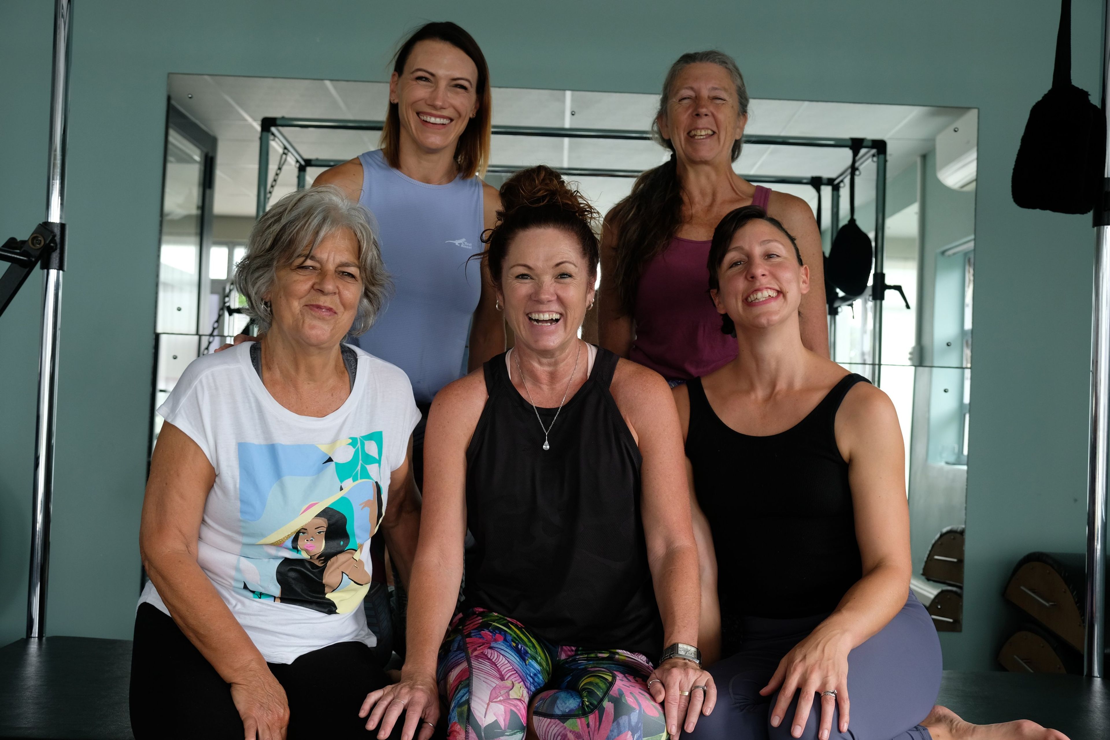 Five instructors laughing together in a close group portrait inside the studio