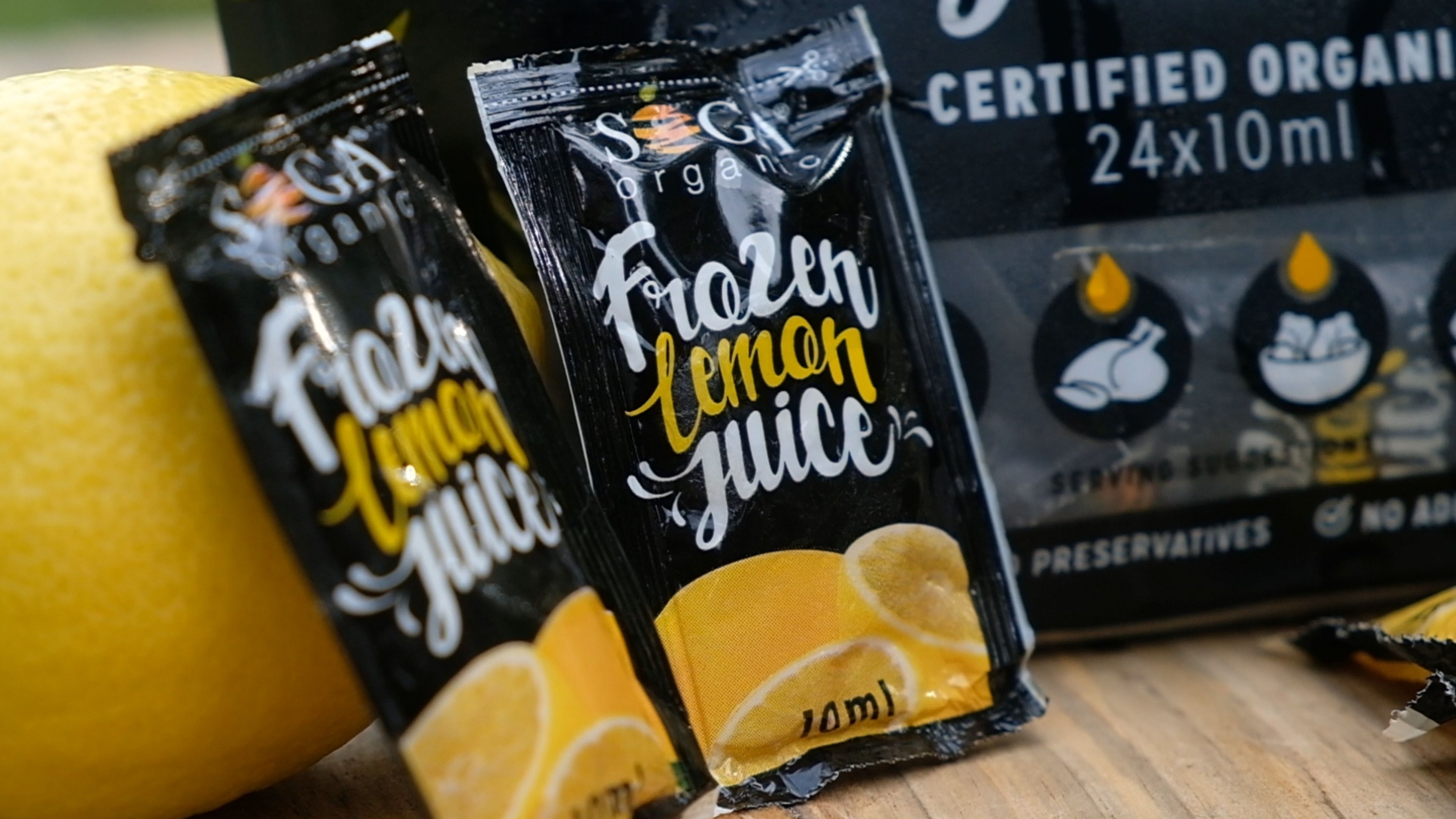 Frozen lemon juice sachets leaning against a lemon in front of the sachet pack
