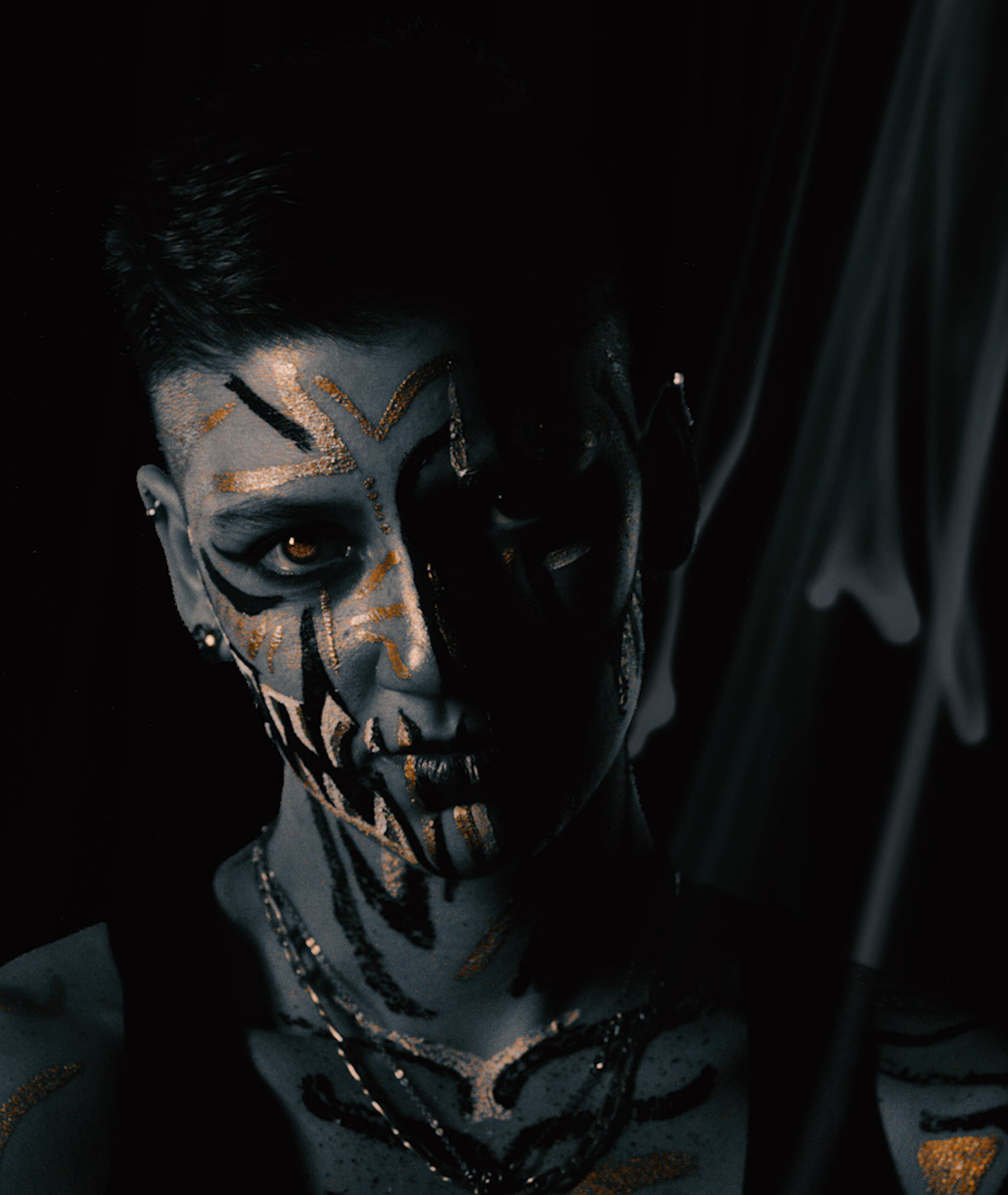 Face-painted portrait with black fang markings and gold, half in shadow on a dark background