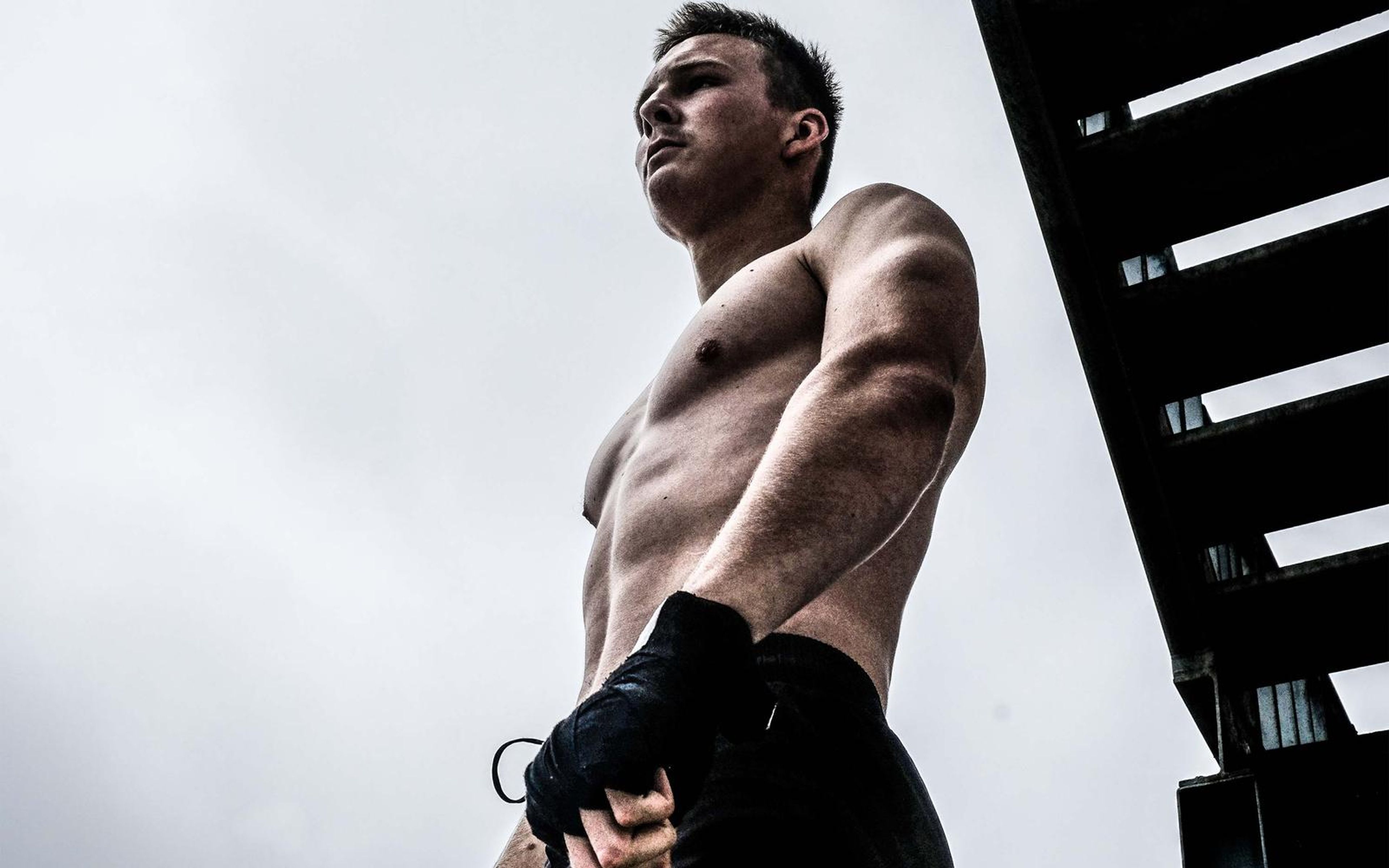 Low angle portrait of a man looking away, arms down with wrapped hands, black stair frame beside him
