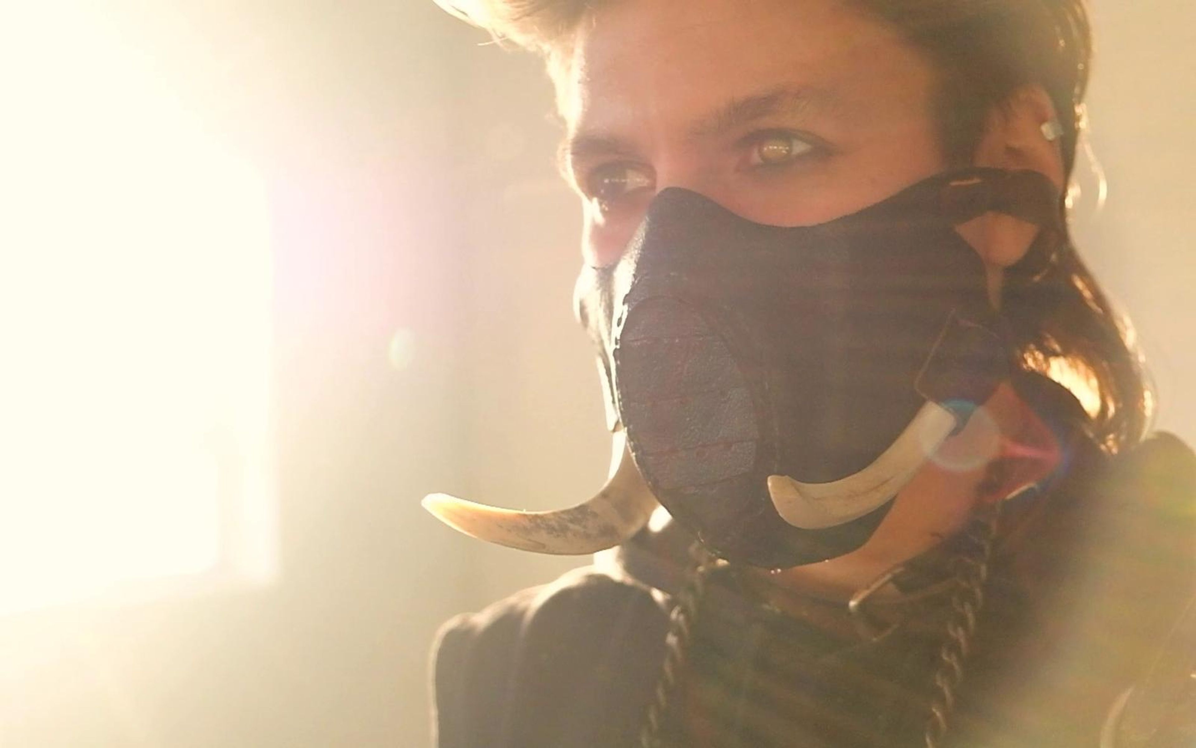 Tilted close portrait of the warrior in the tusked mask with golden lens flare across the frame