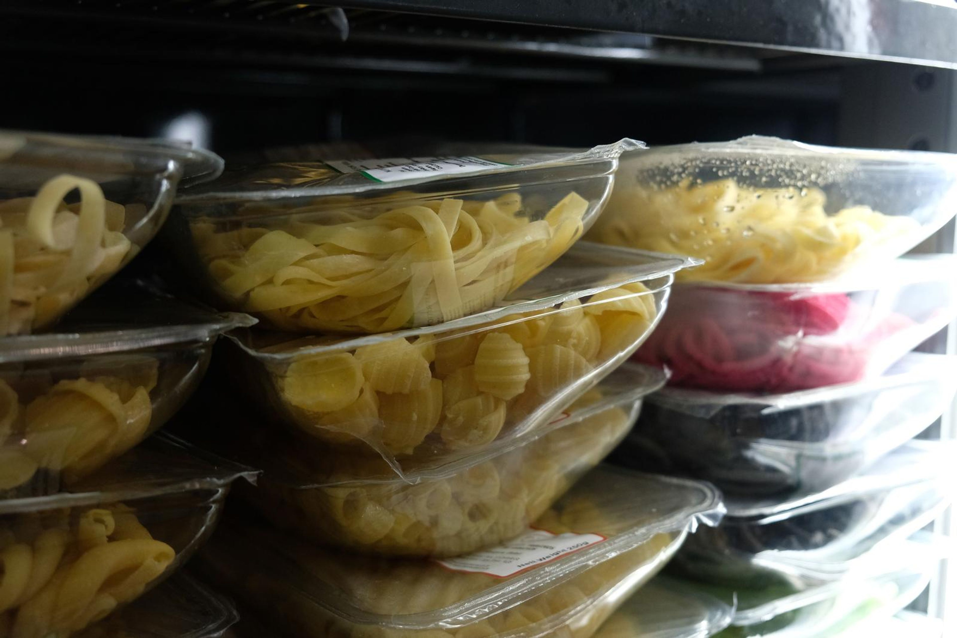 Stacked clear bowls of fresh pasta shapes in the fridge