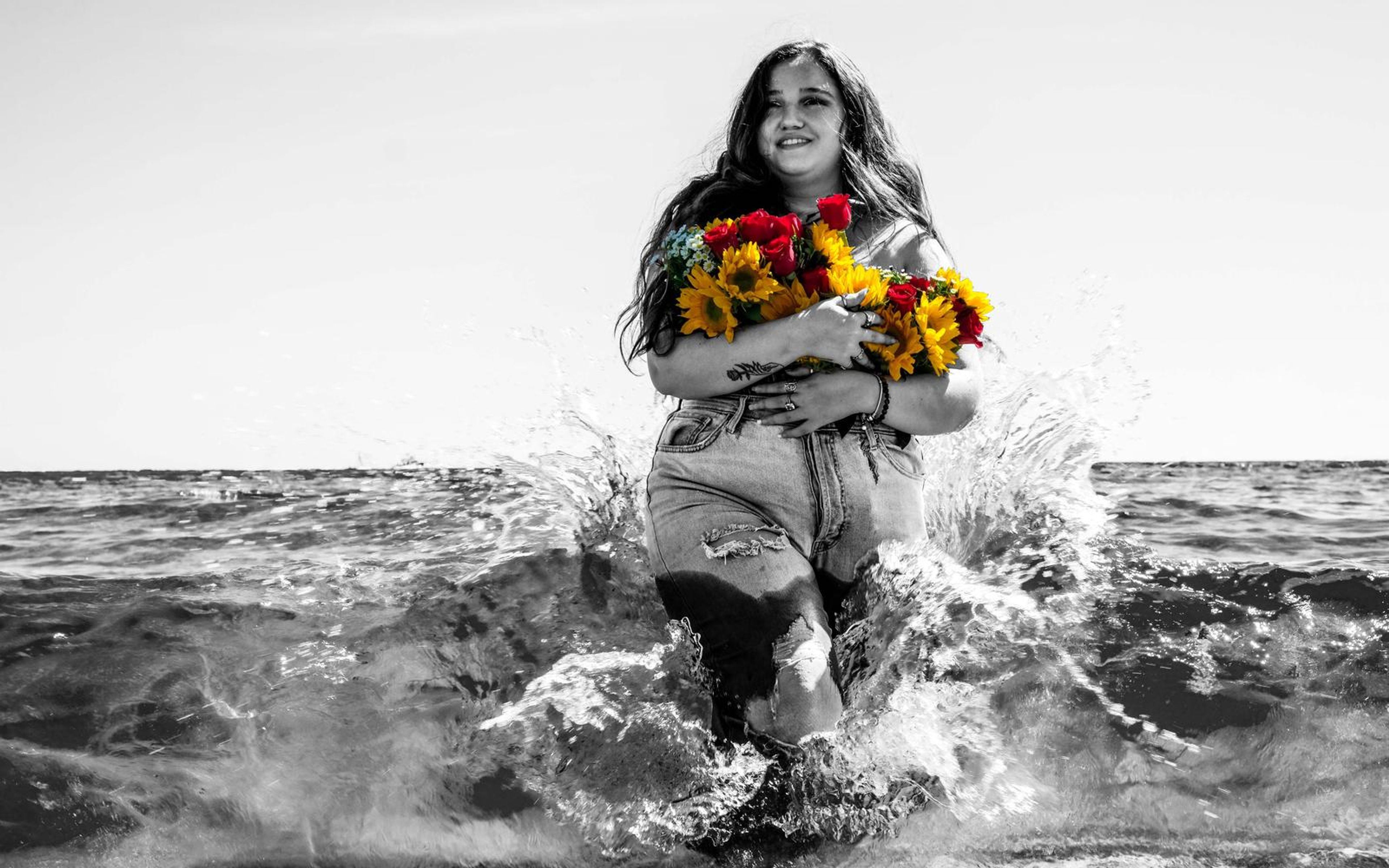Black and white wide shot of model walking through churning water, bouquet held close, hair swept back