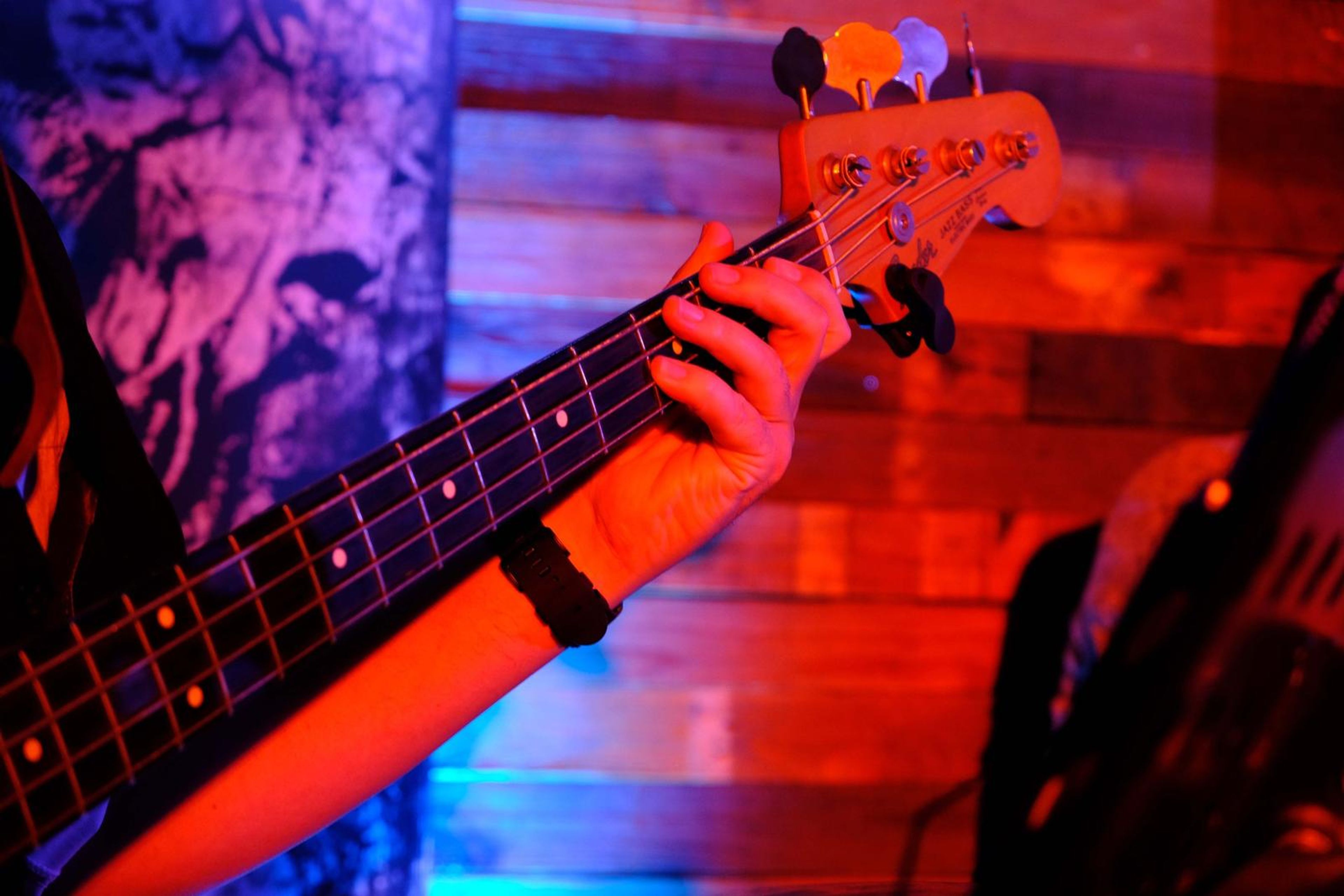 Close-up of a bassist's hand on the neck of a bass guitar in red light