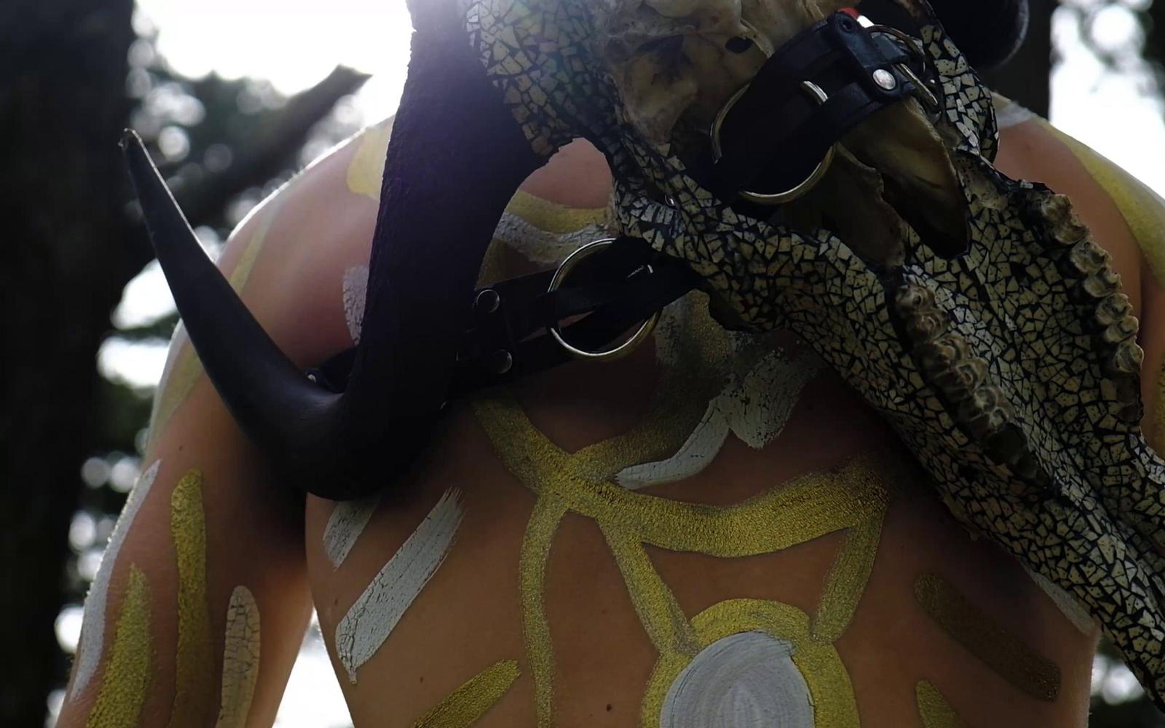 Low angle of the performer with the horned skull and painted shoulders against sunlit pines
