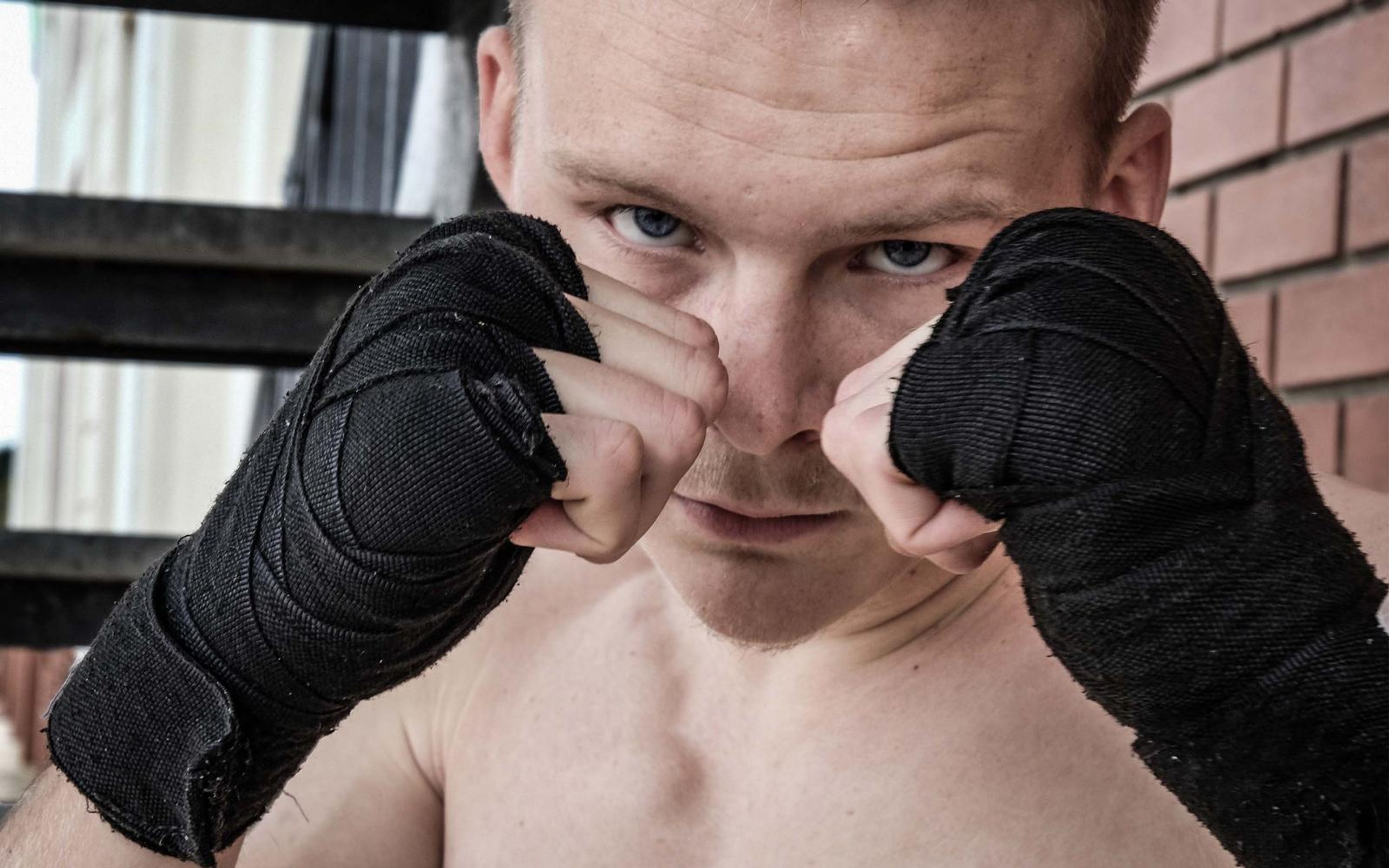 Fighter with both wrapped fists up guarding his face and staring into the lens in front of a brick wall