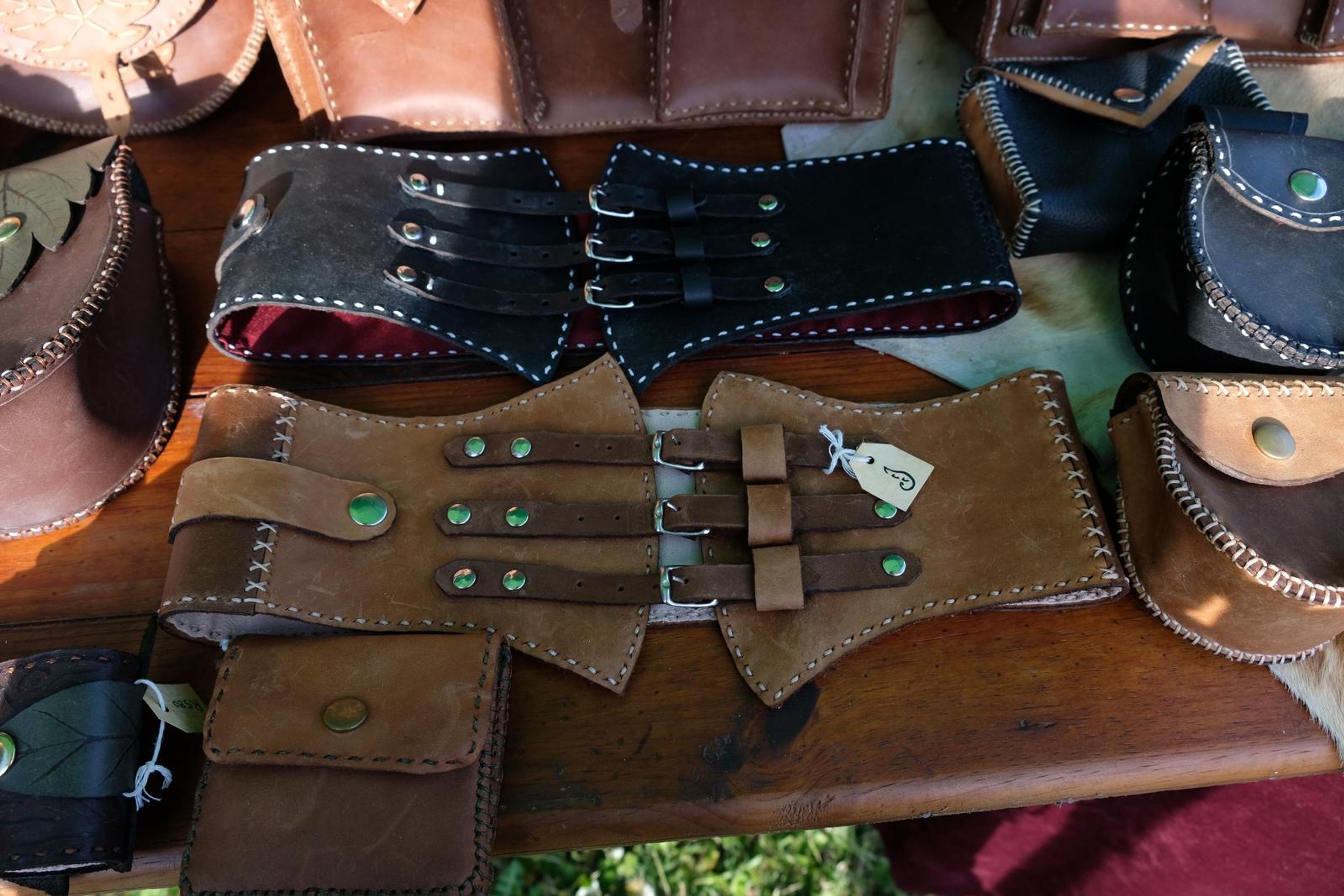 Tan and black leather corset belts and satchels laid out at the Juuks stall