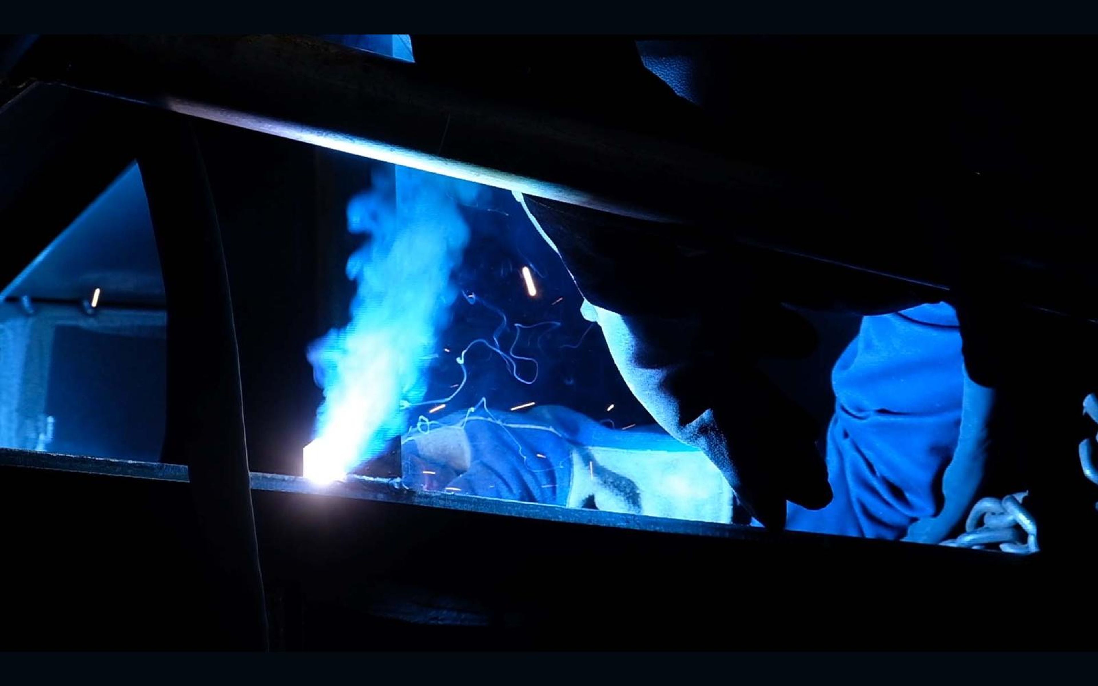 Welder leaning over steel with a blue arc and sparks