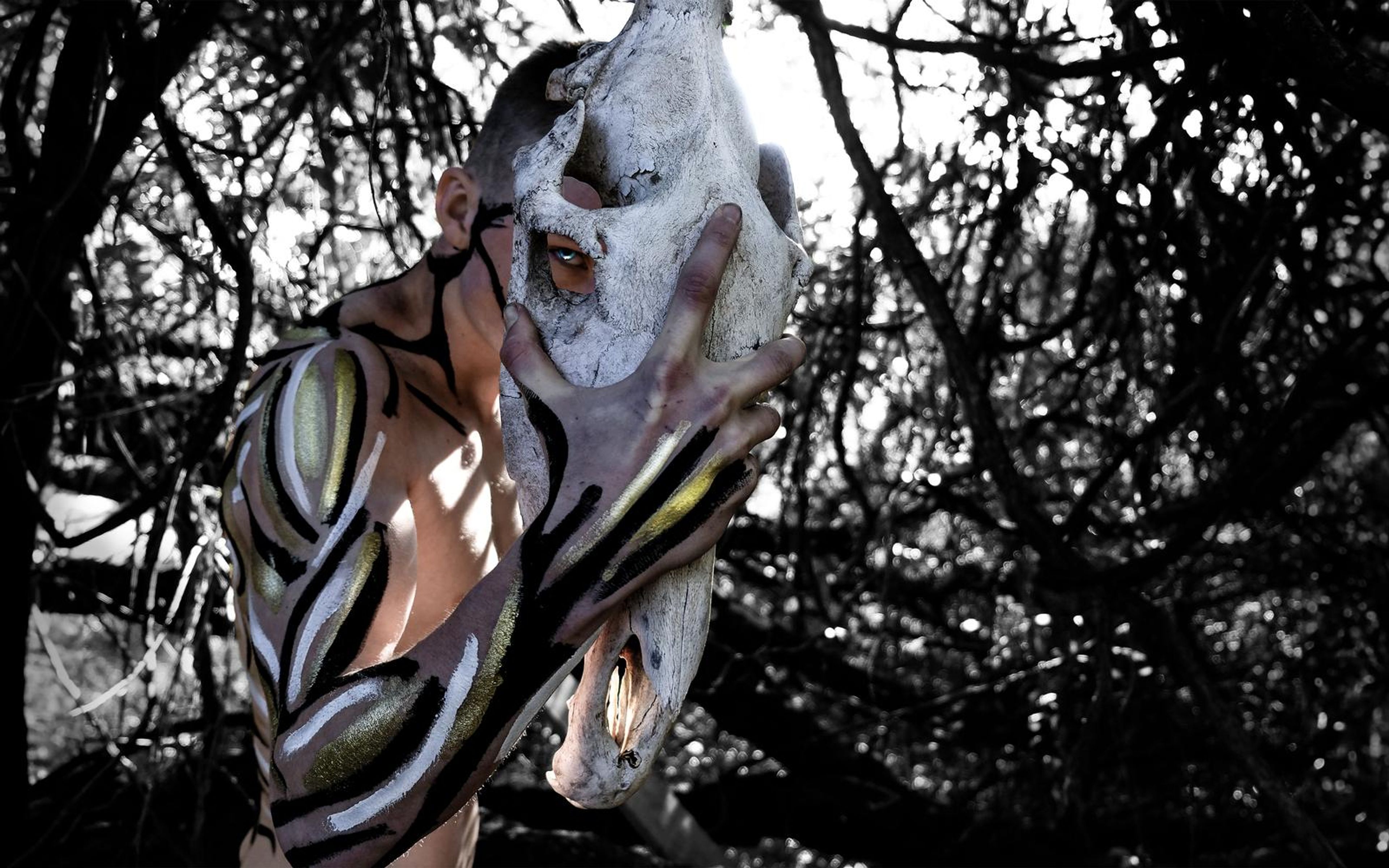 Performer in tiger-stripe body paint pressing his face to a large white skull in a tangle of branches