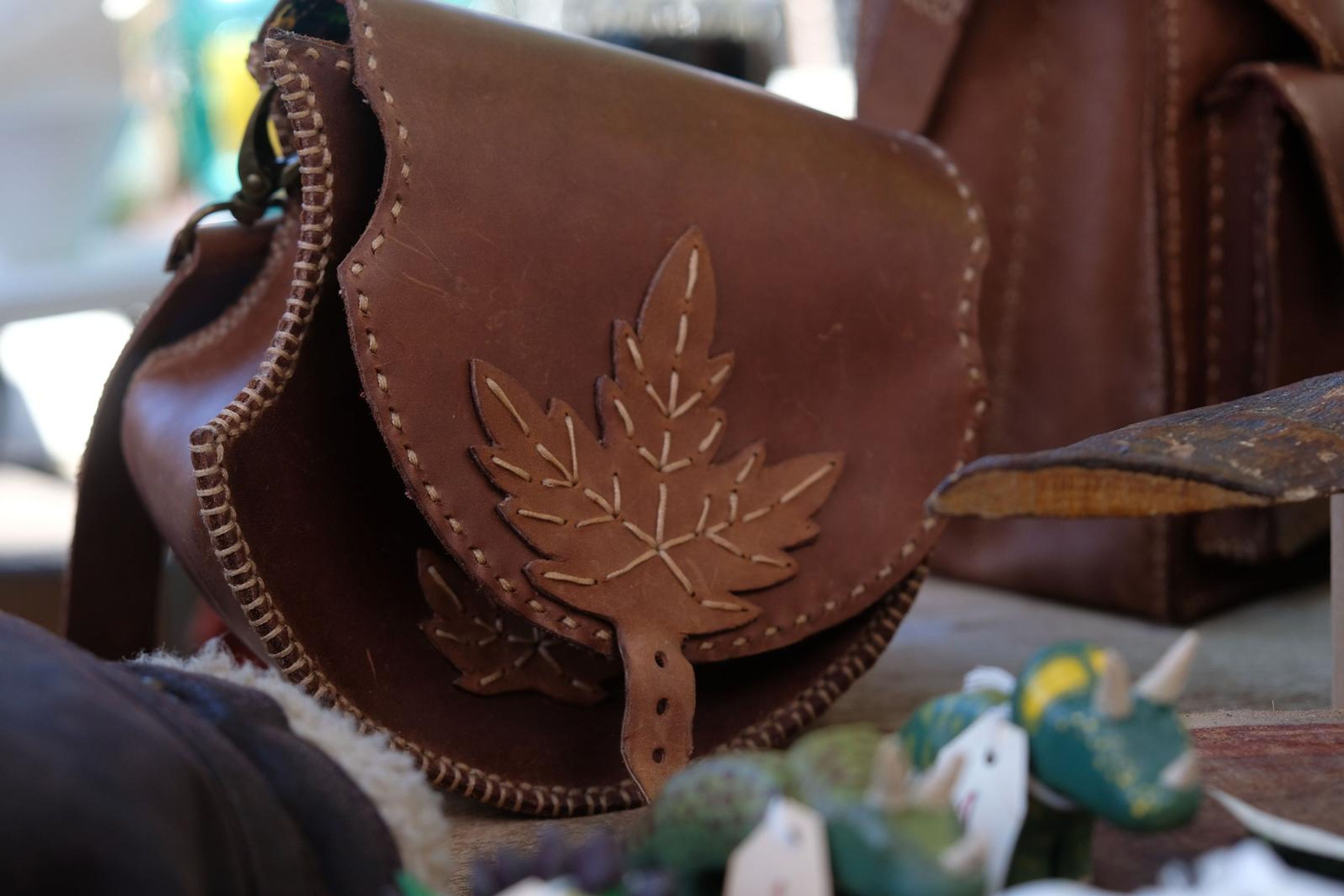 Brown leather pouch with a pressed maple leaf design and stitched edge