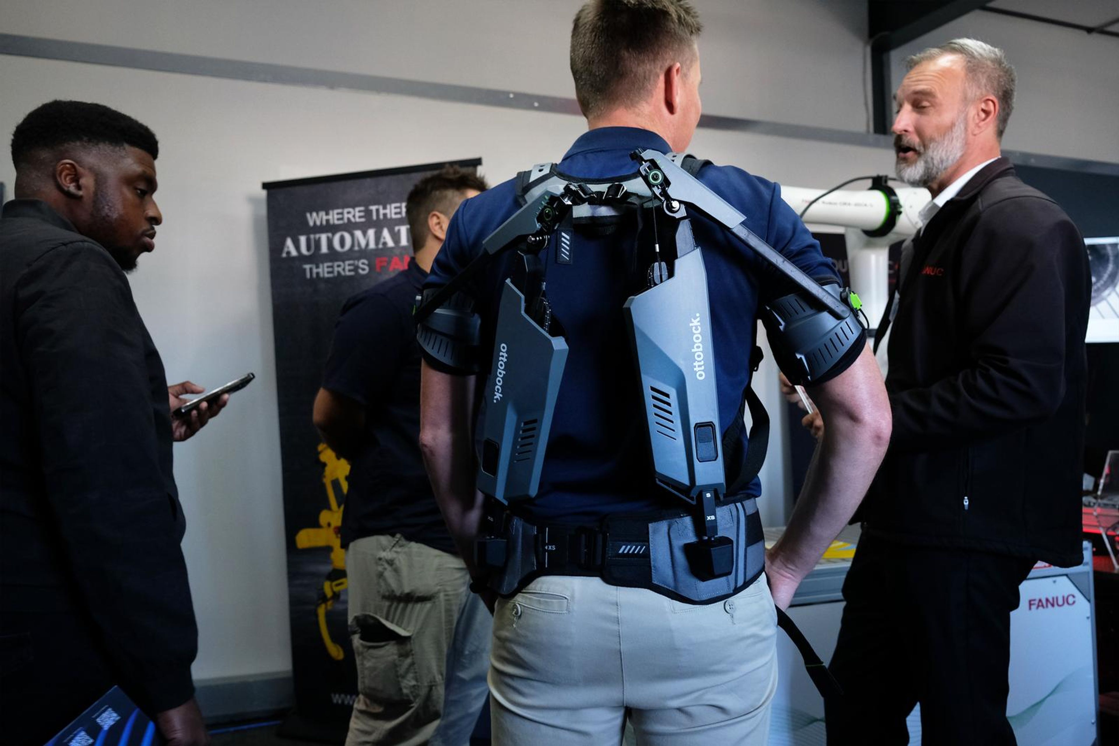 Visitor wearing the exoskeleton while talking with two men at the SuitX stand