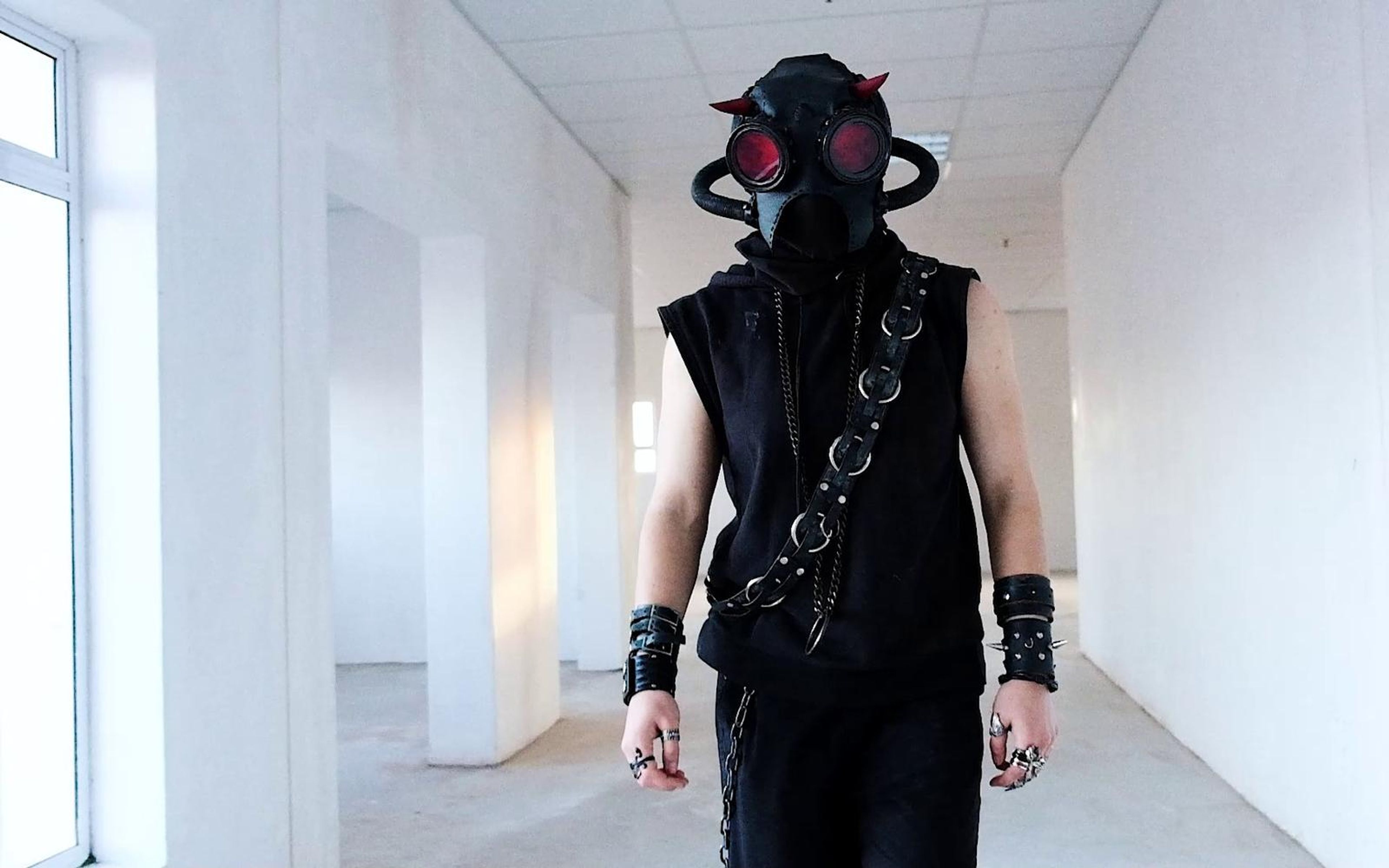 Warrior in a horned gas mask with red lenses standing in a white corridor beside tall windows