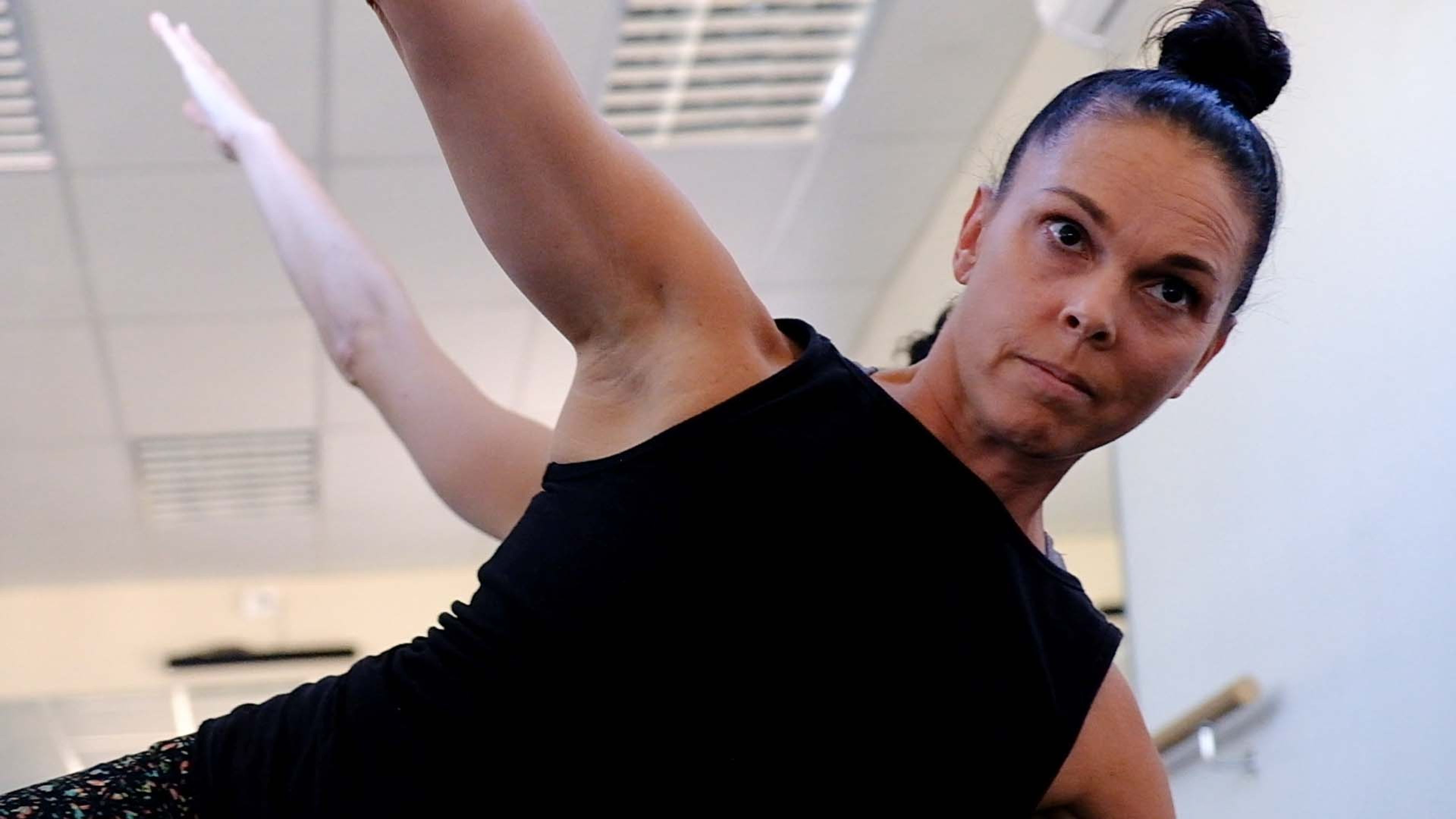 Instructor in a black top in a side stretch, looking at the camera