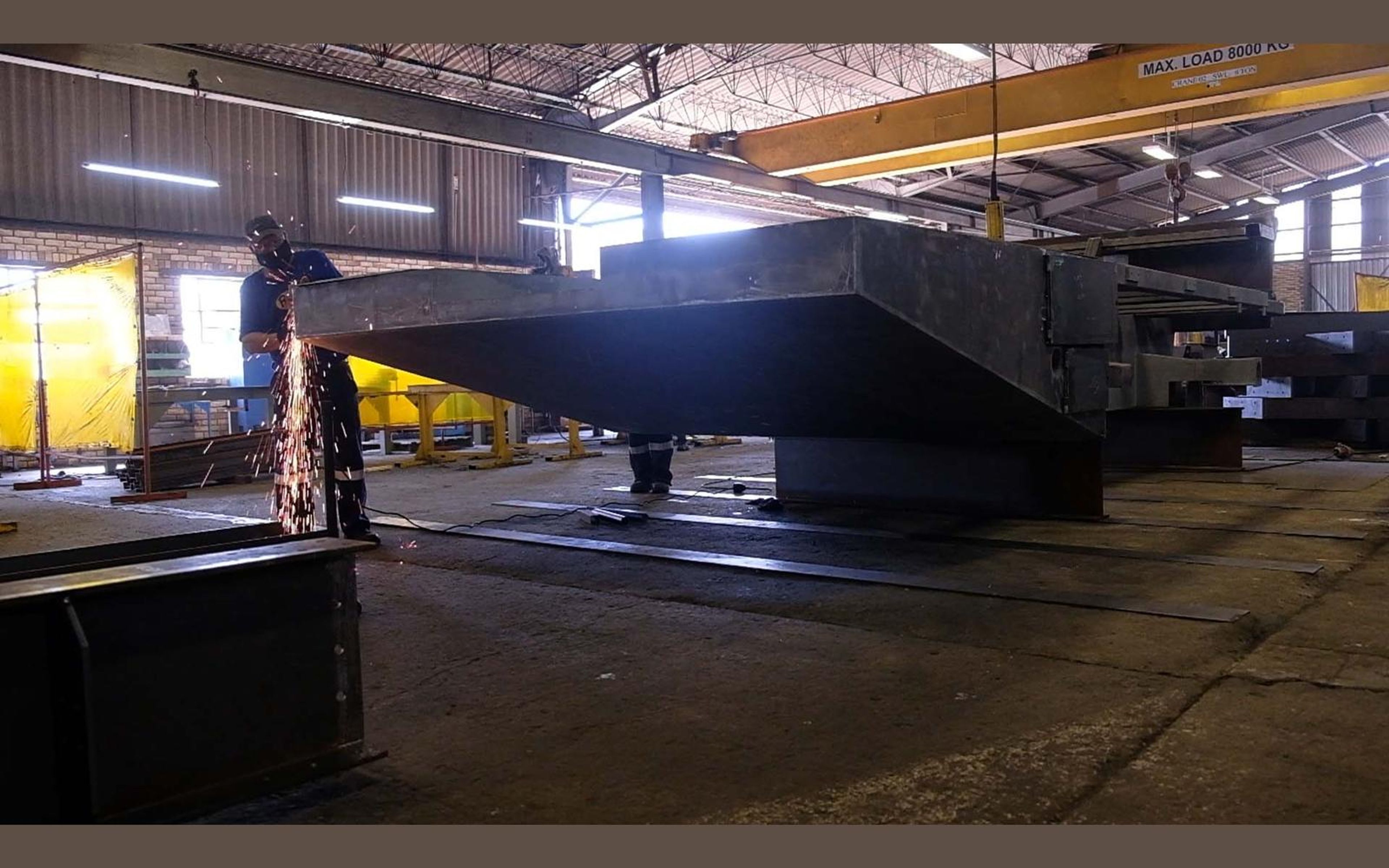 Fabricators at work among steel beams in the shop