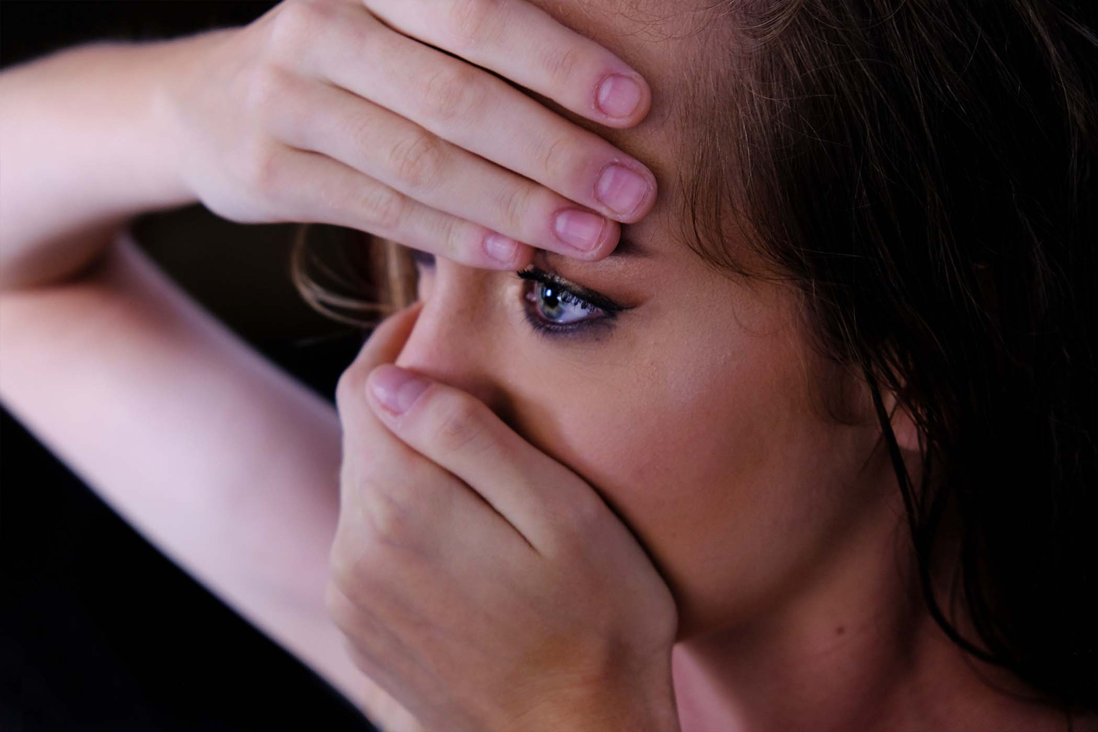 Close-up portrait, hands framing the face, eye makeup visible through fingers