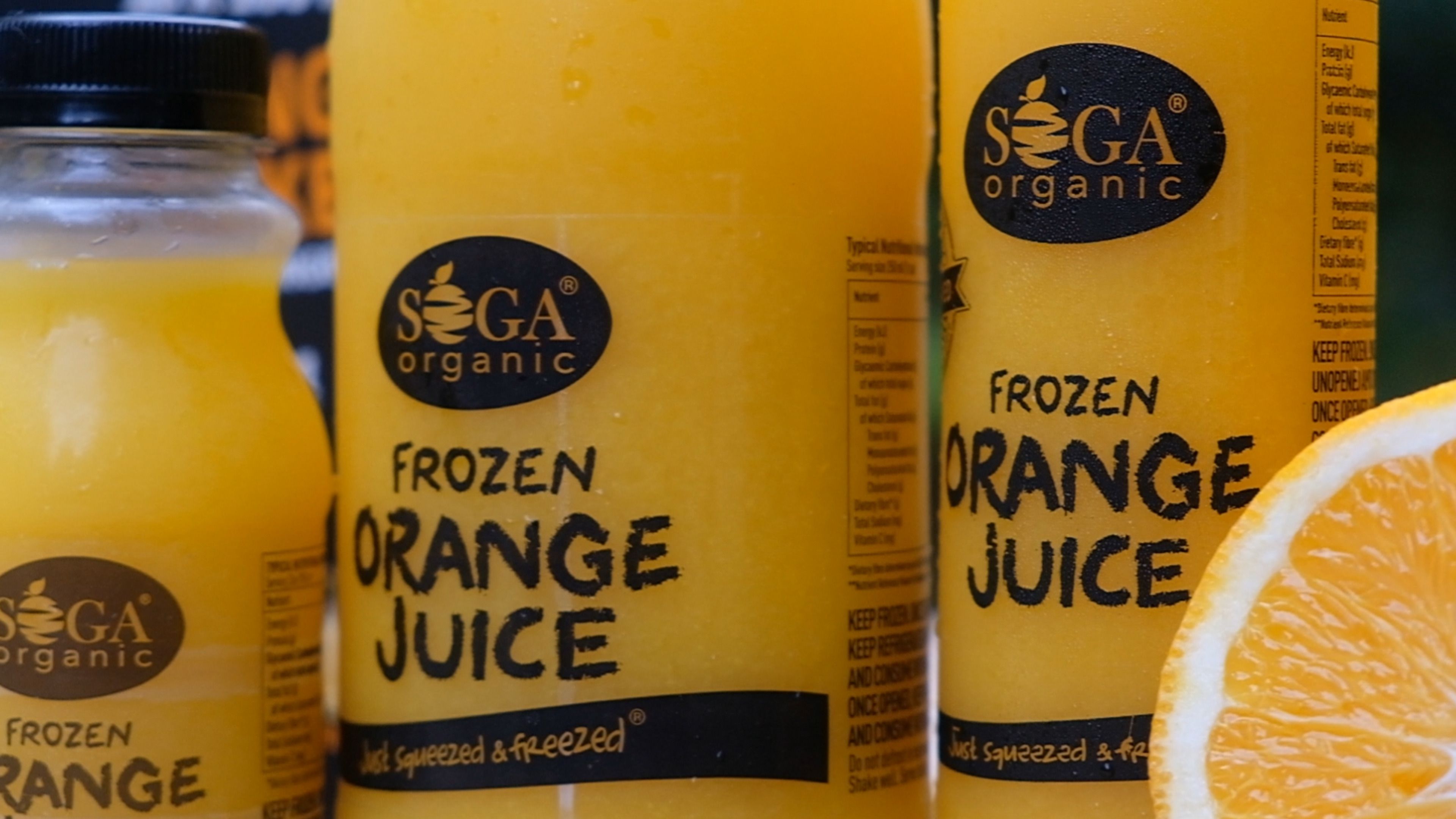 Close-up of SOGA frozen orange juice bottle labels beside an orange half