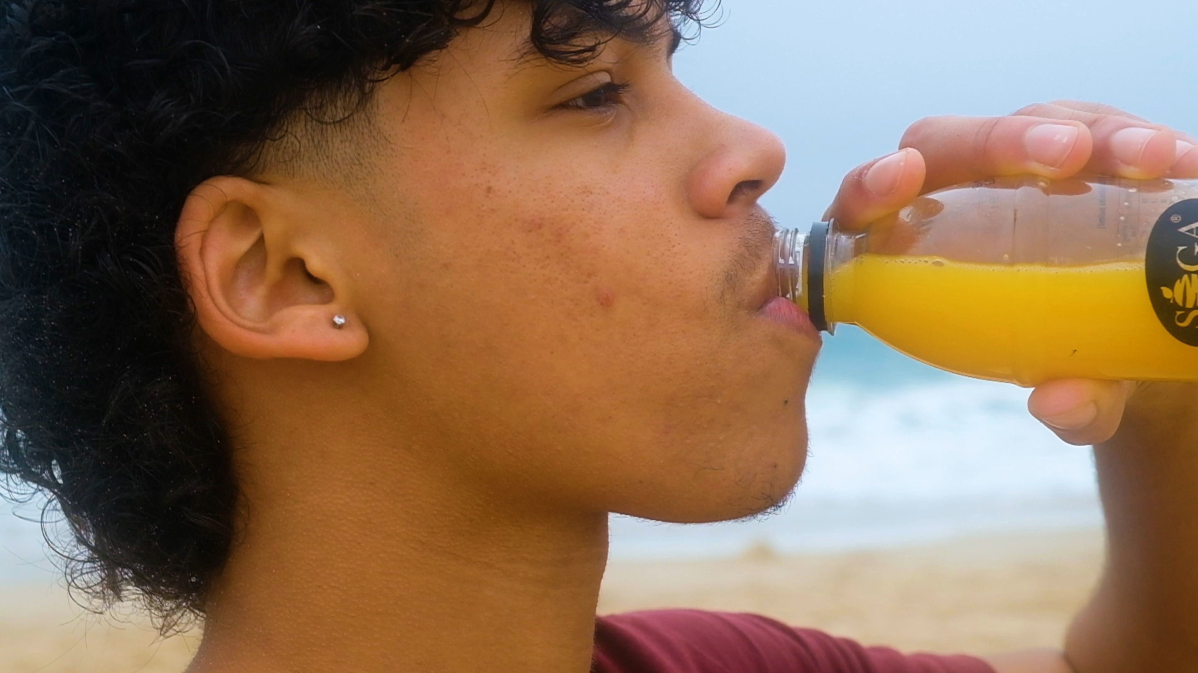 Young man drinking SOGA orange juice on the beach