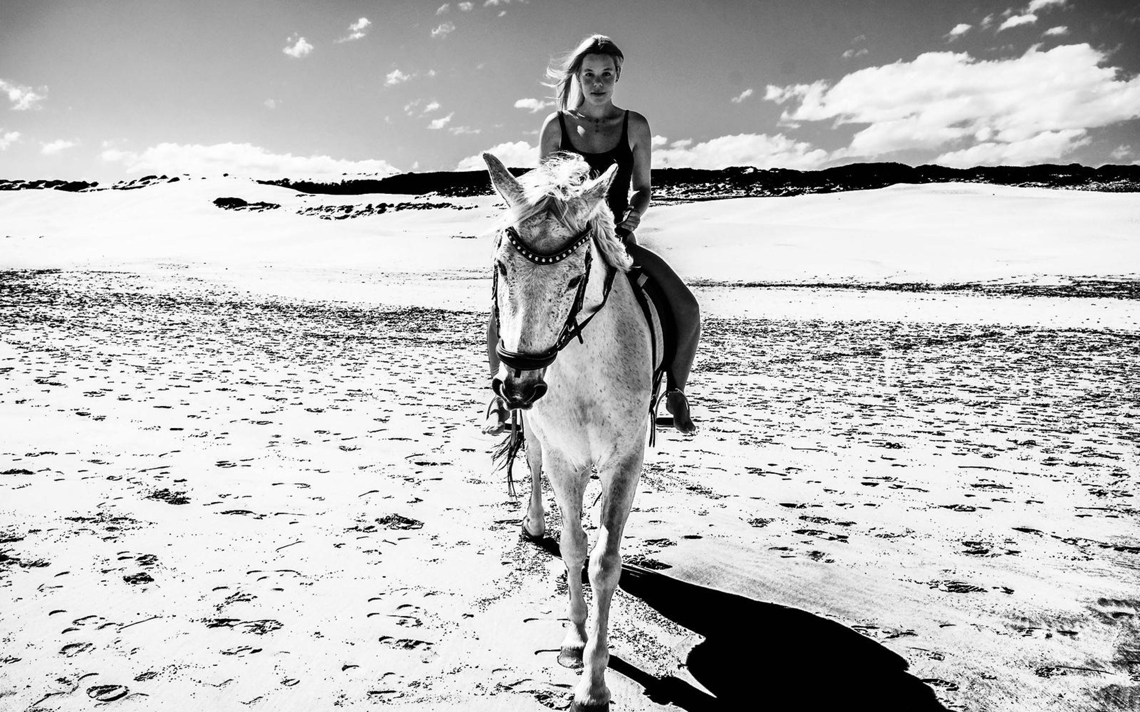 Black and white high-contrast edit of a woman riding a white horse toward the camera