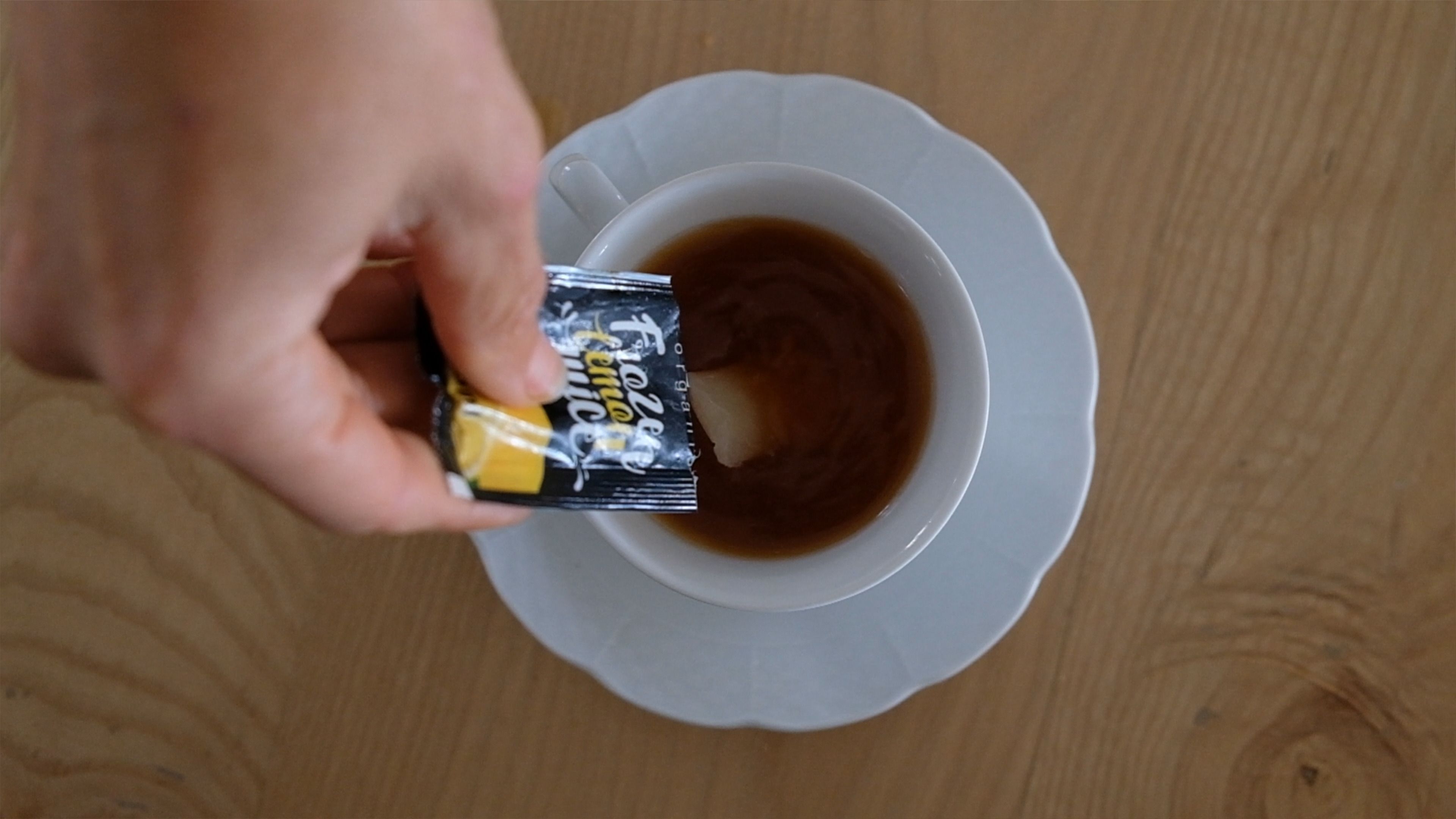 Hand holding a lemon juice sachet over a cup of tea