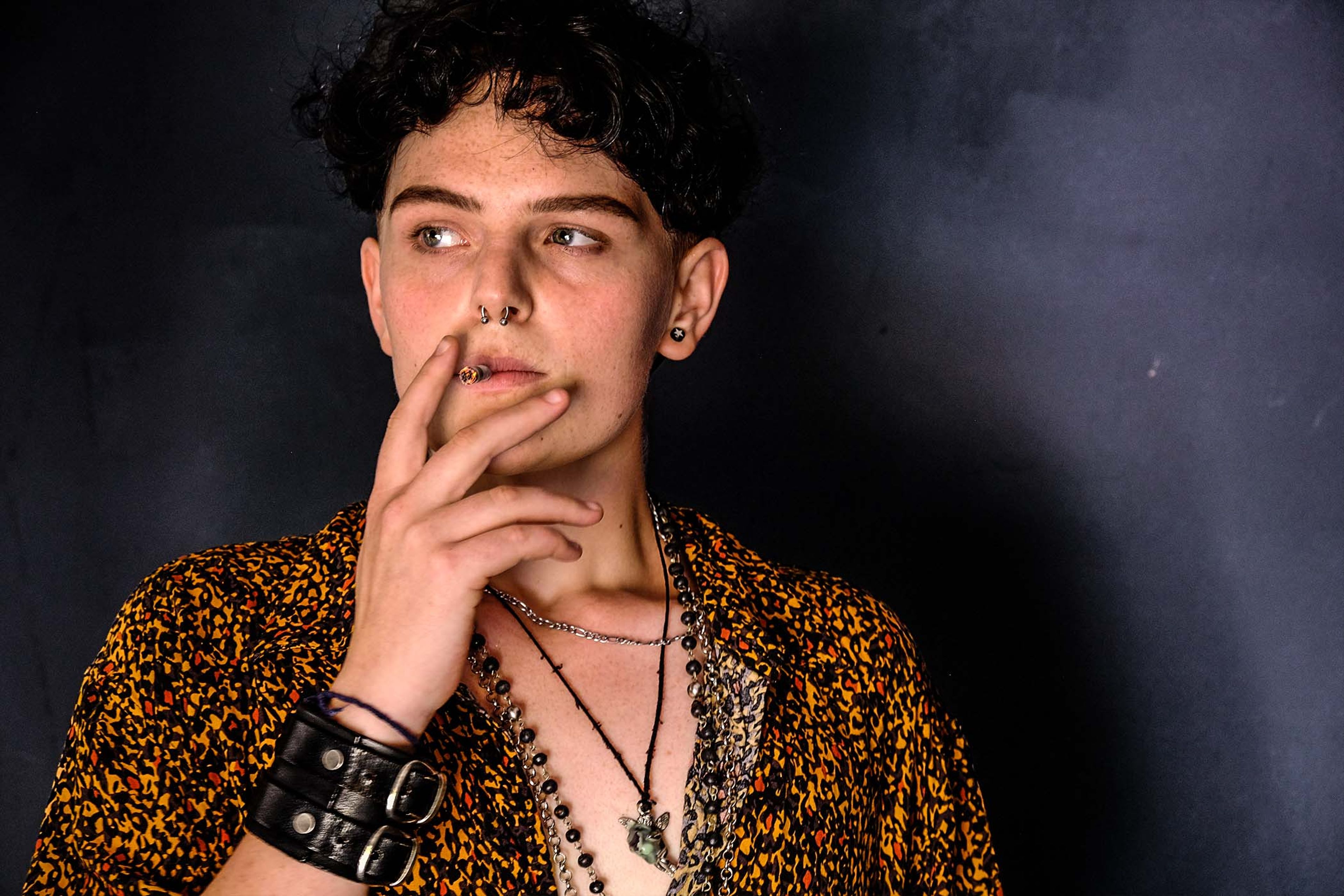 Close-up portrait, subject in a patterned shirt and leather wrist cuff, hand resting near the chin