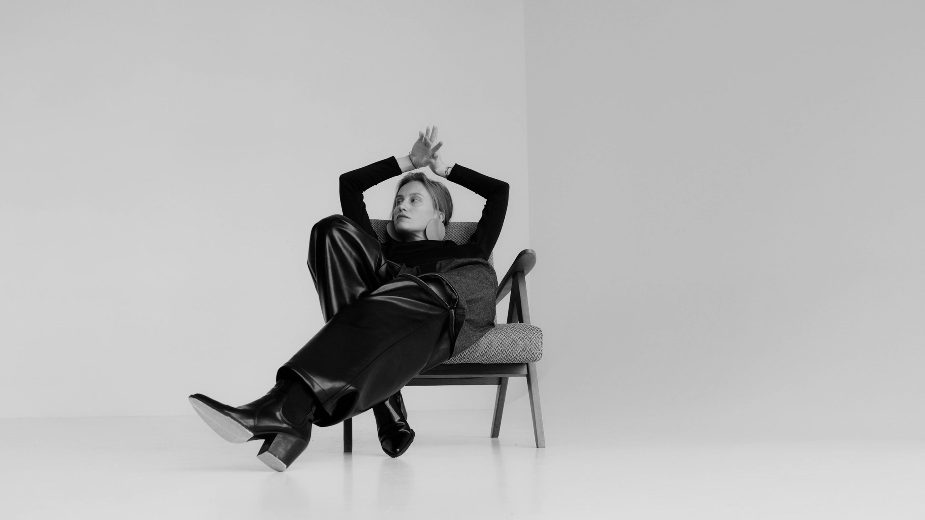 Woman in black reclining on a modern chair against a white studio wall