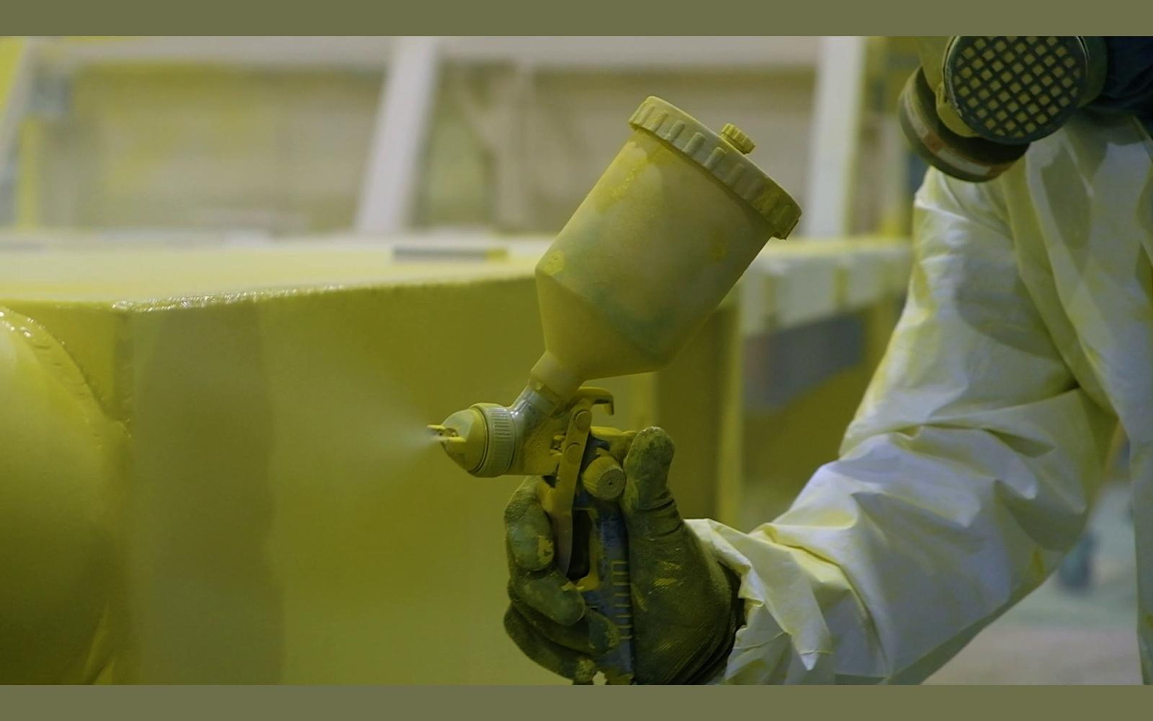 Spray gun with a cup of yellow paint held against a steel panel