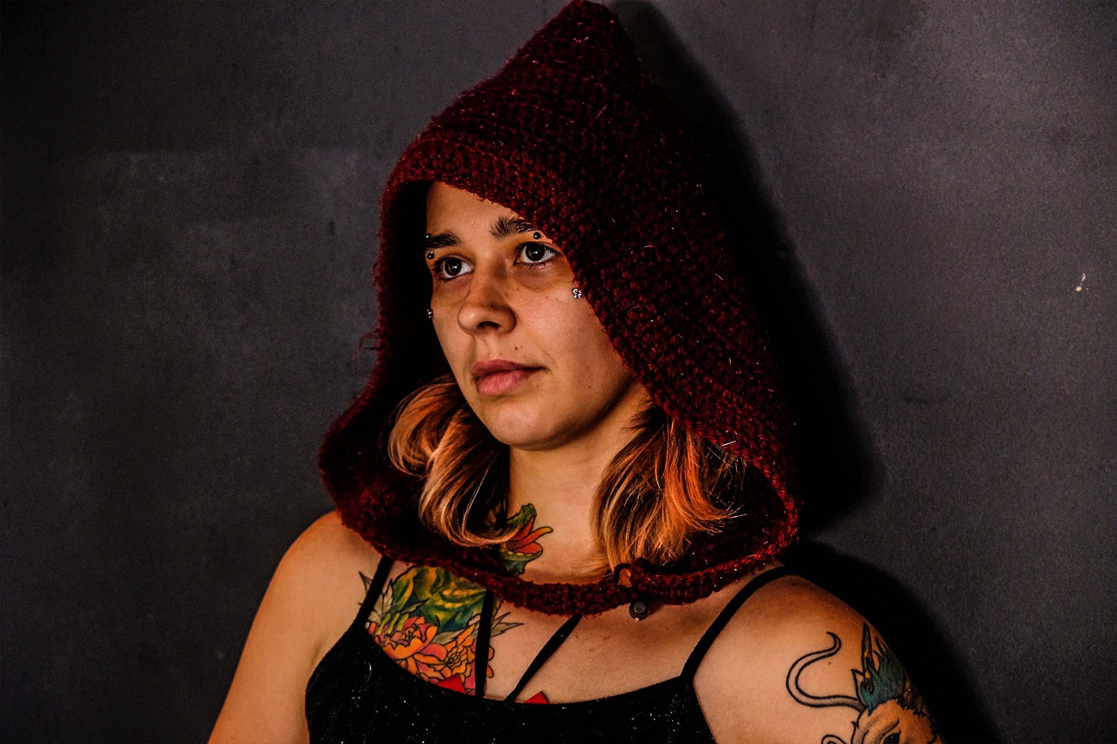 Portrait, subject in a maroon knit hood looking off camera, tattoos visible on the chest