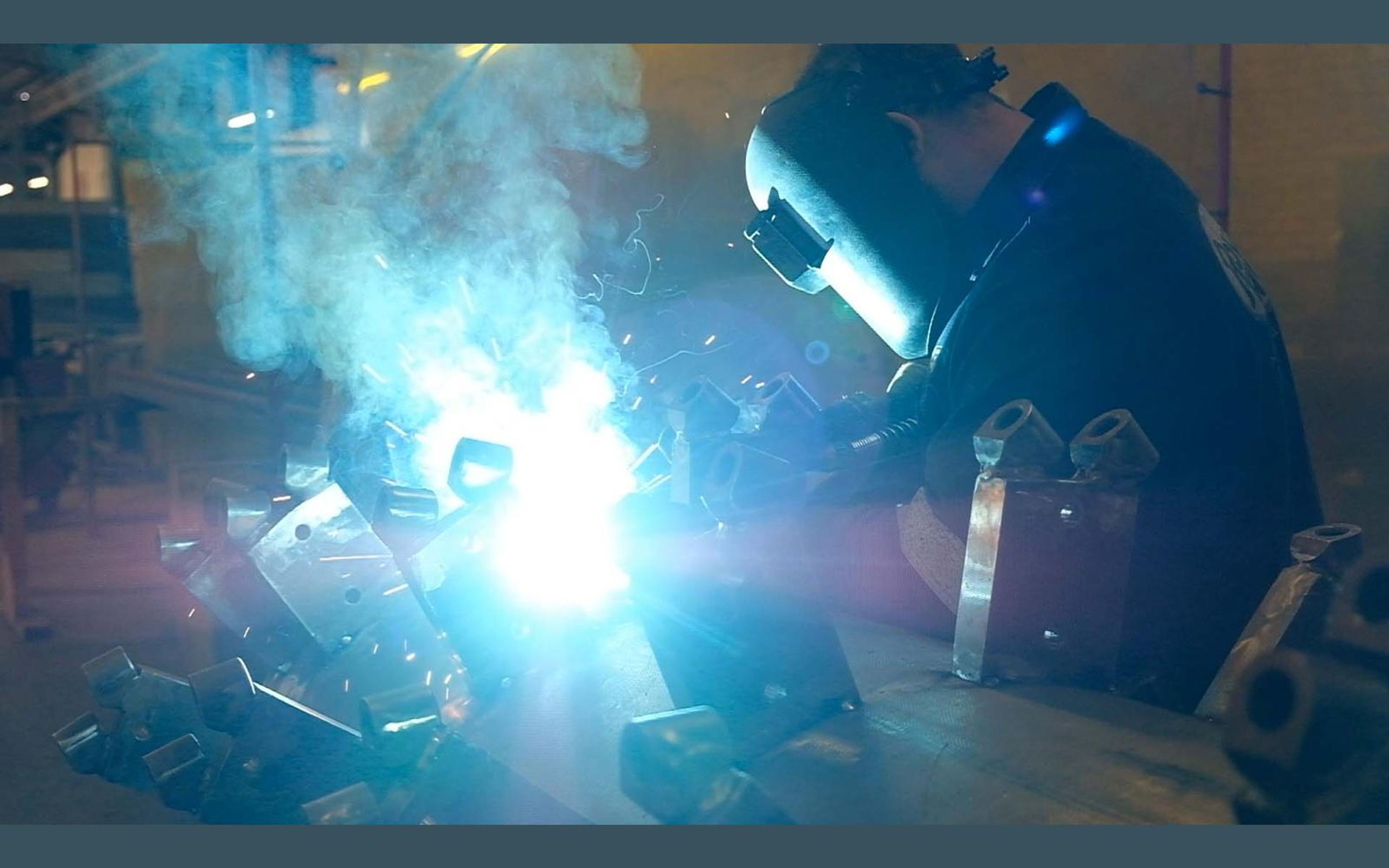 Welder in a helmet with sparks and smoke over steel brackets