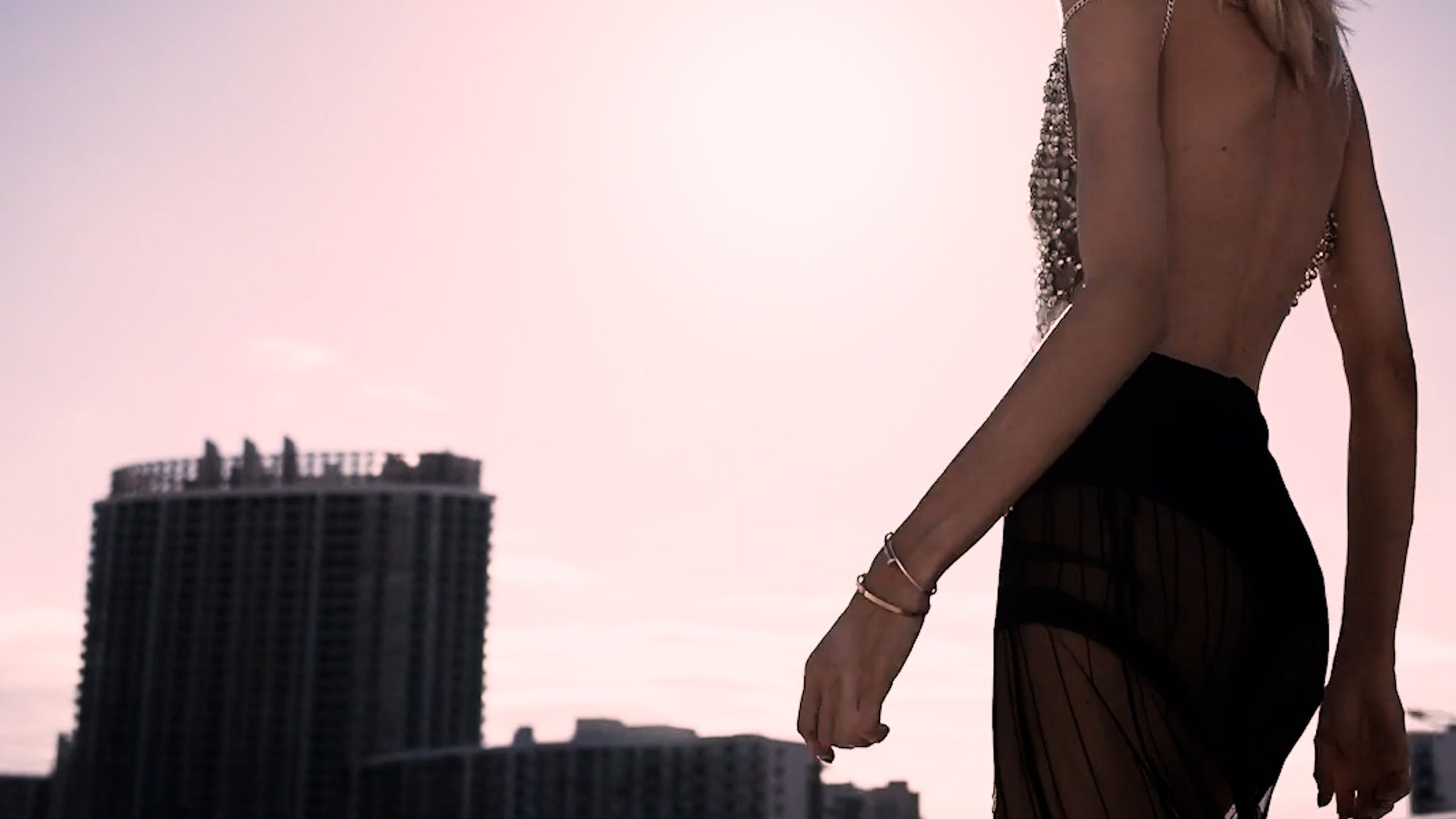 Woman in a sheer black skirt walking against a pink sunset skyline