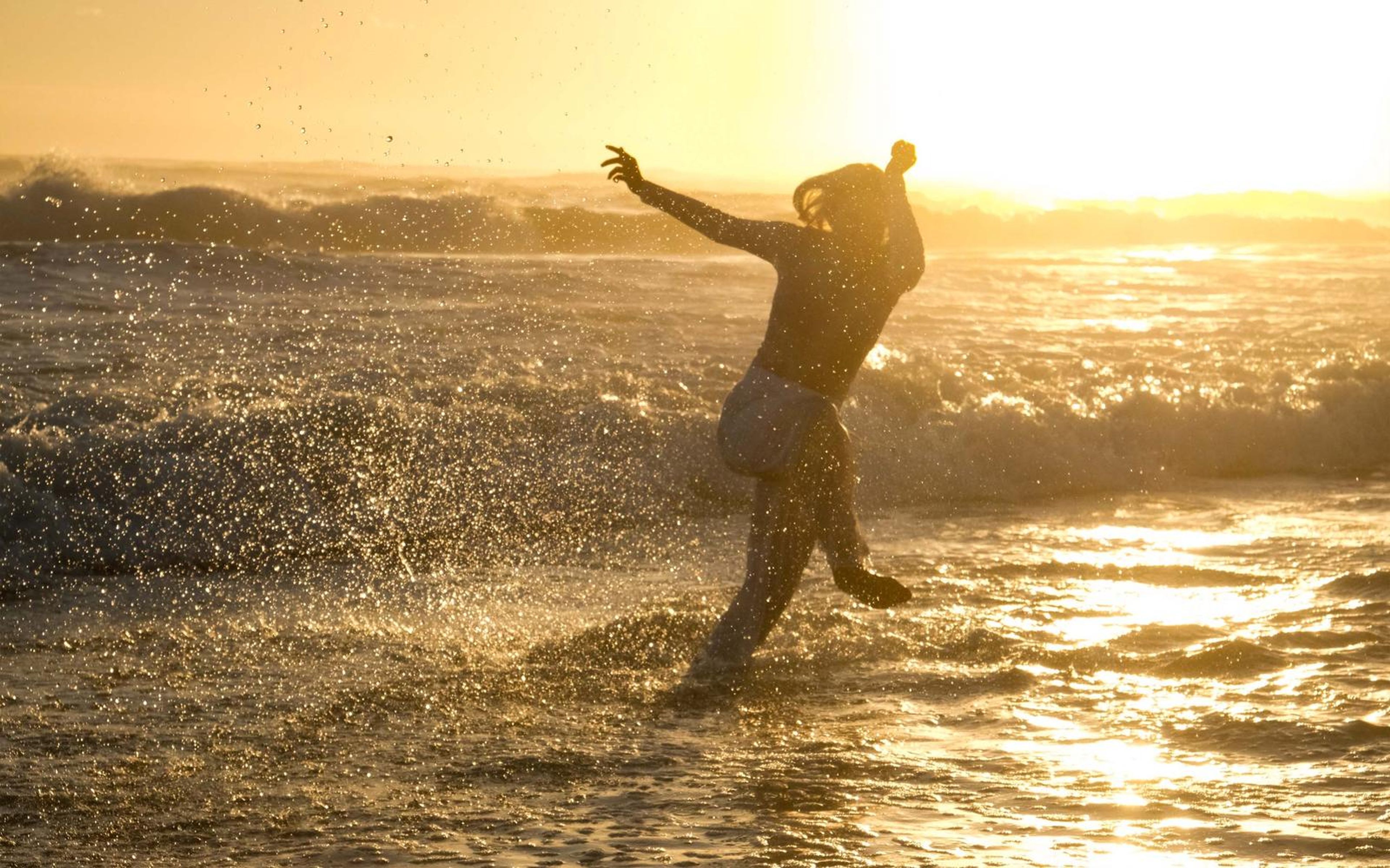 Dancer mid leap in the shallows at sunset, spray flying around her