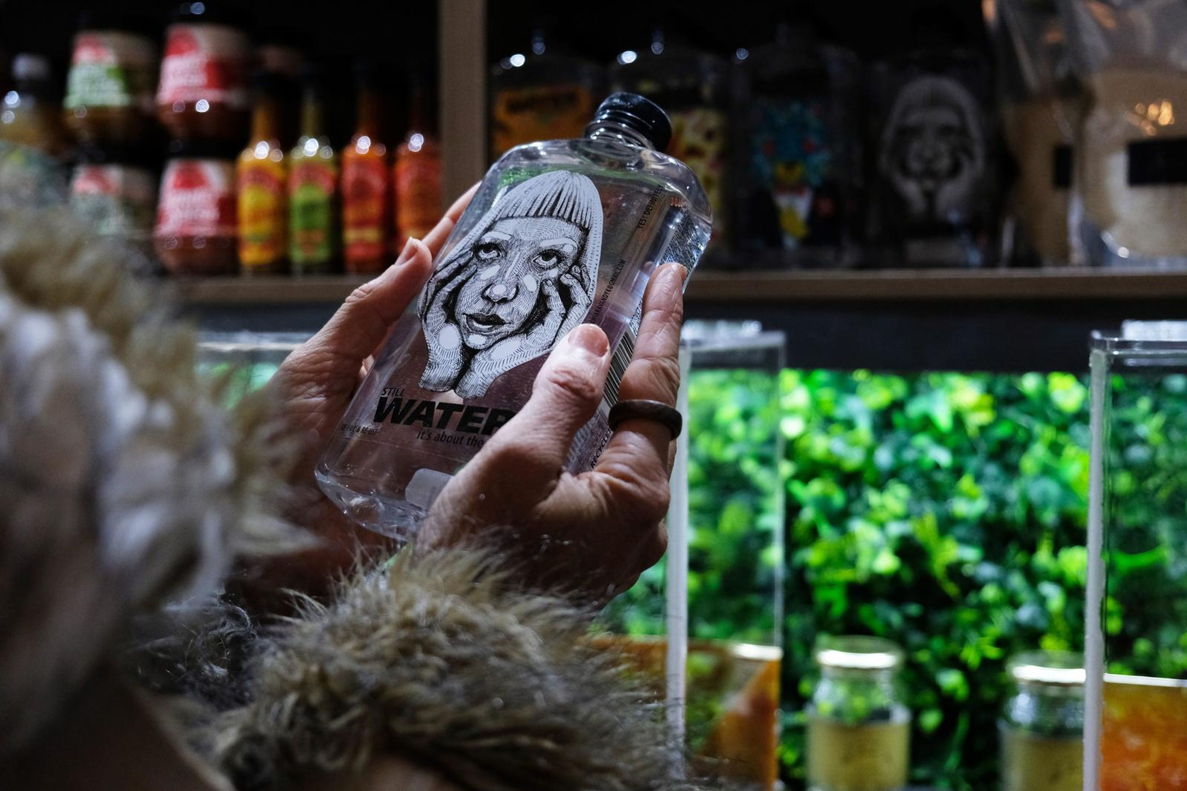 Hands holding a Water bottle with a hand-drawn portrait label