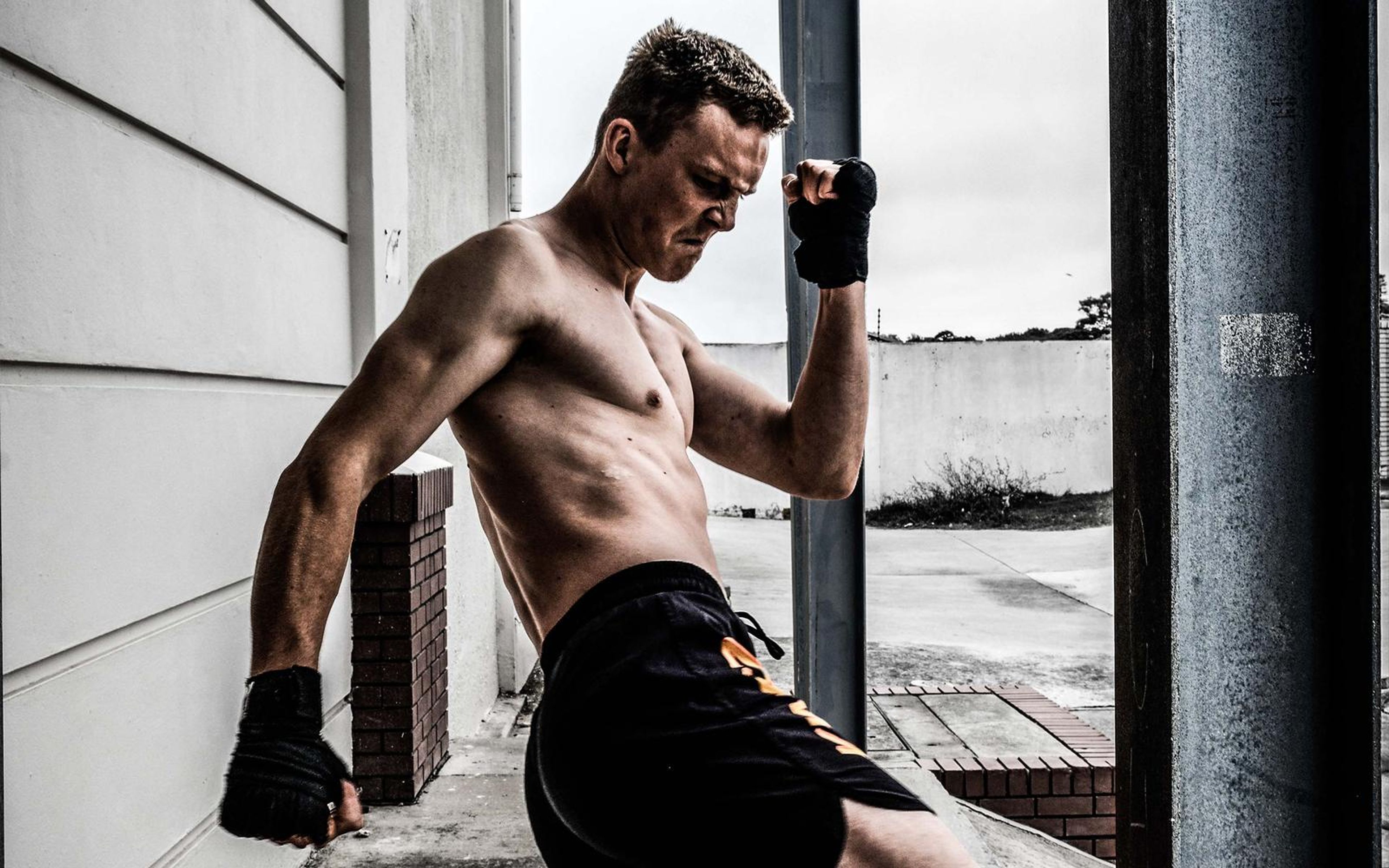 Fighter bracing against a steel pole with his wrapped fist beside his face and head lowered
