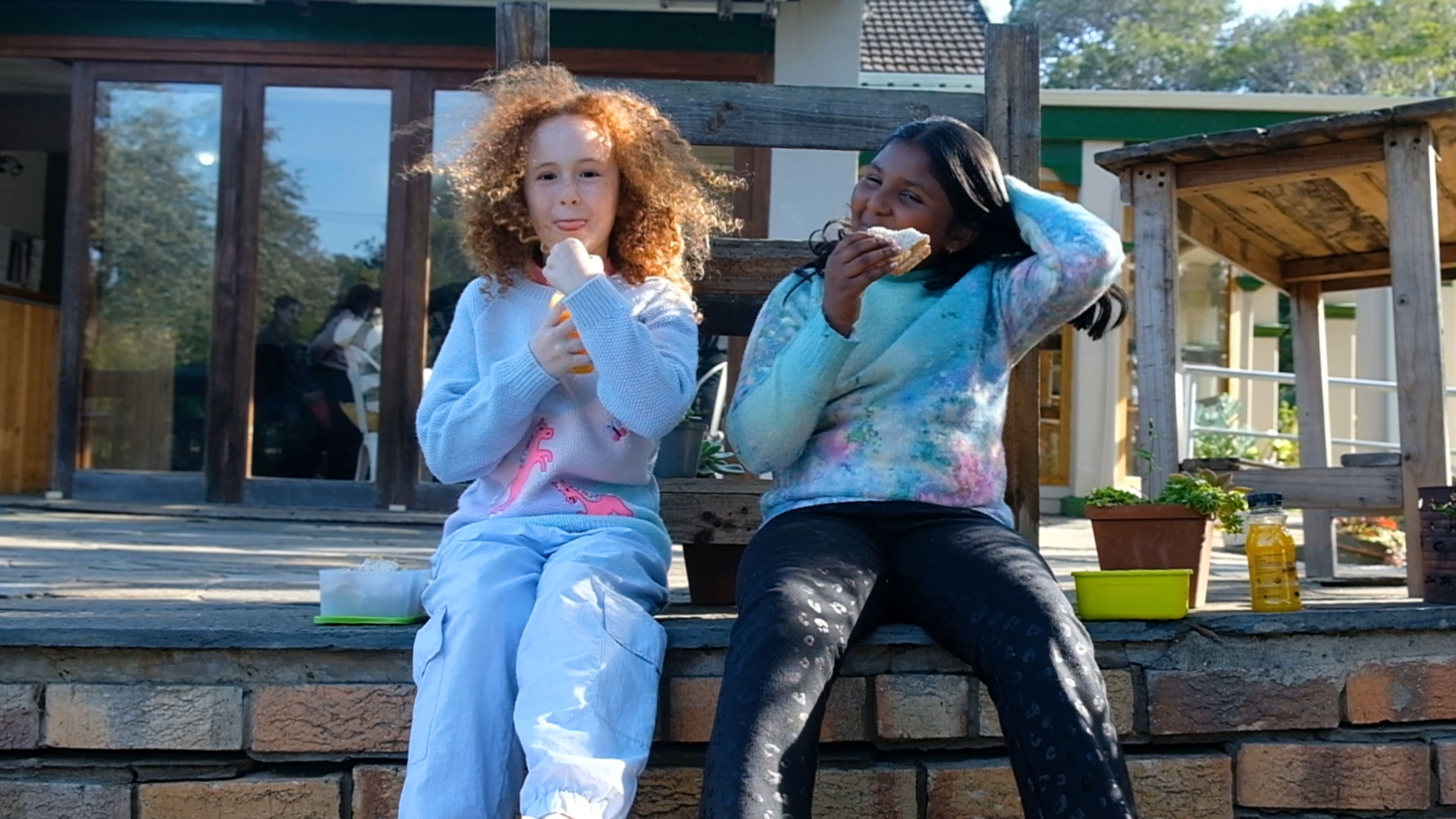 Two girls sitting on a step eating lunch outdoors