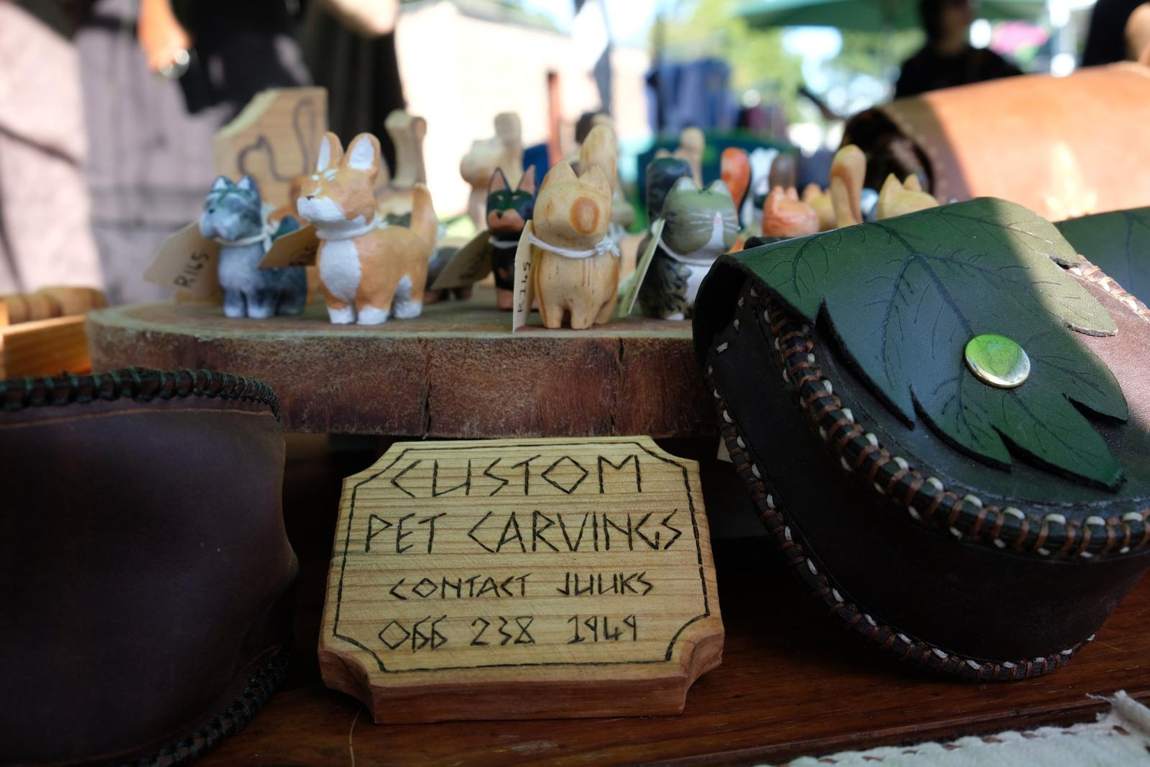 Black leaf-shaped leather pouches beside a Custom Pet Carvings sign