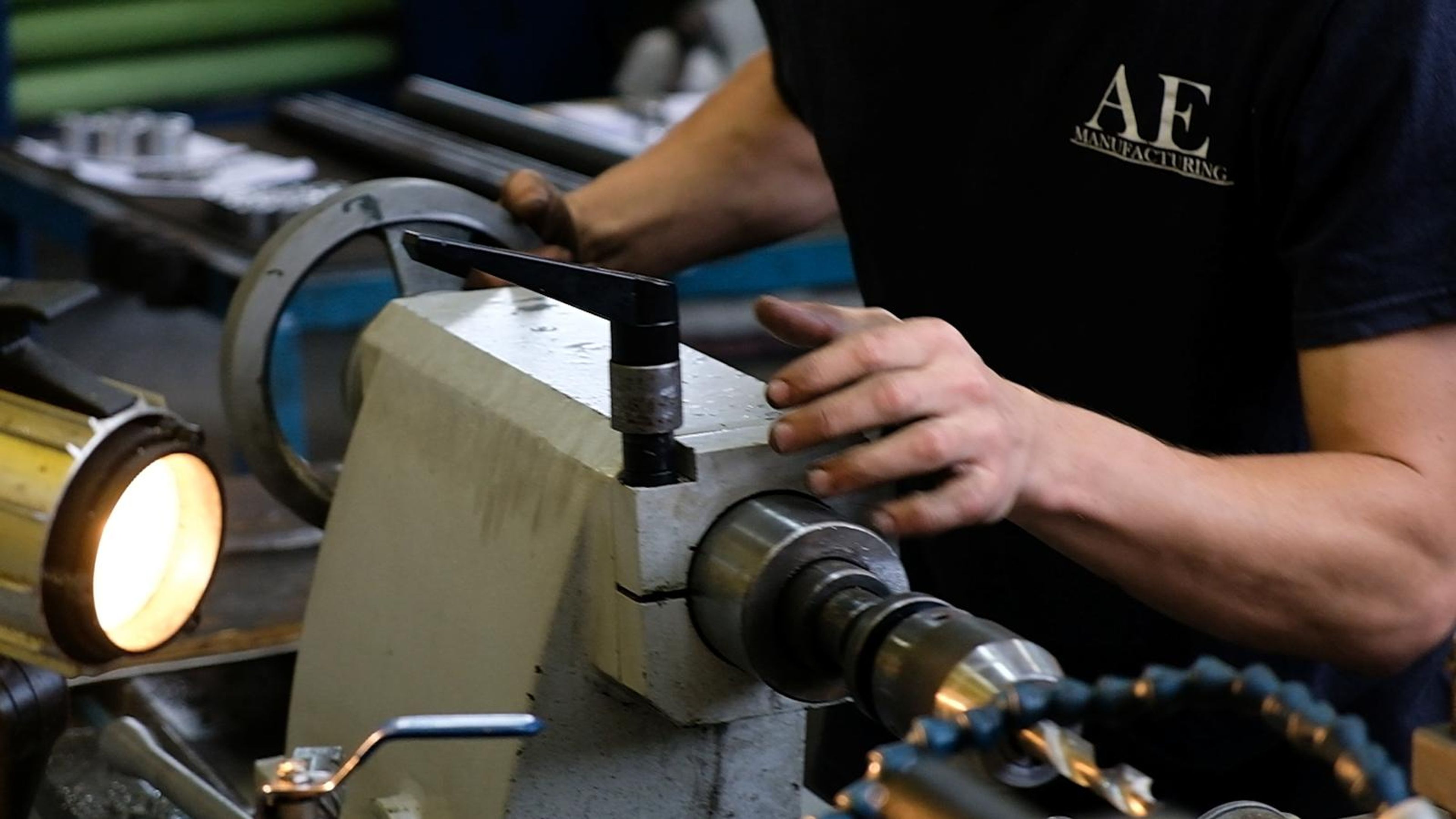 Machinist in an AE shirt with a hand on a lathe control