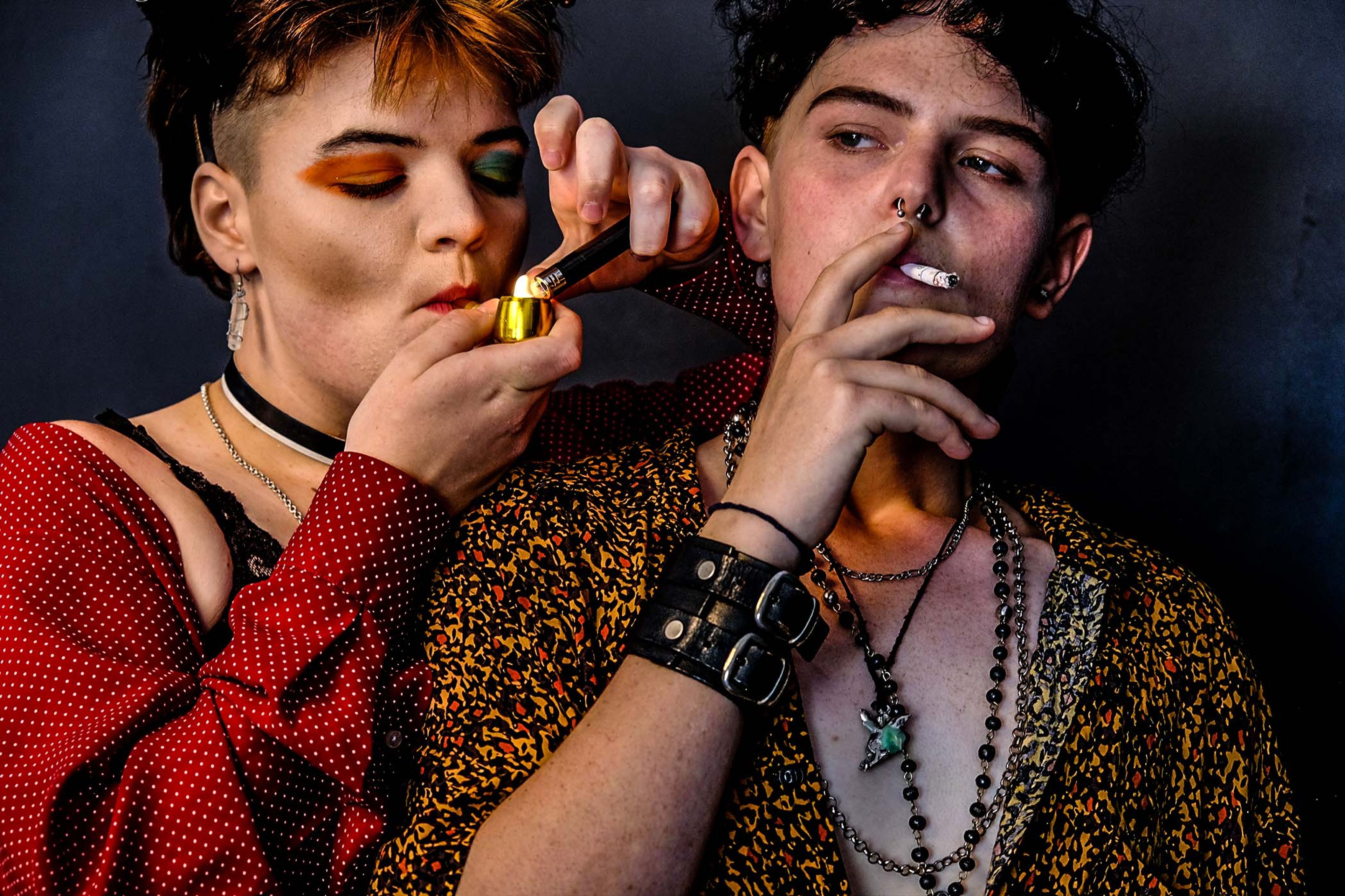 Portrait of a couple, one lighting the other's cigarette, colorful eye makeup and patterned shirts