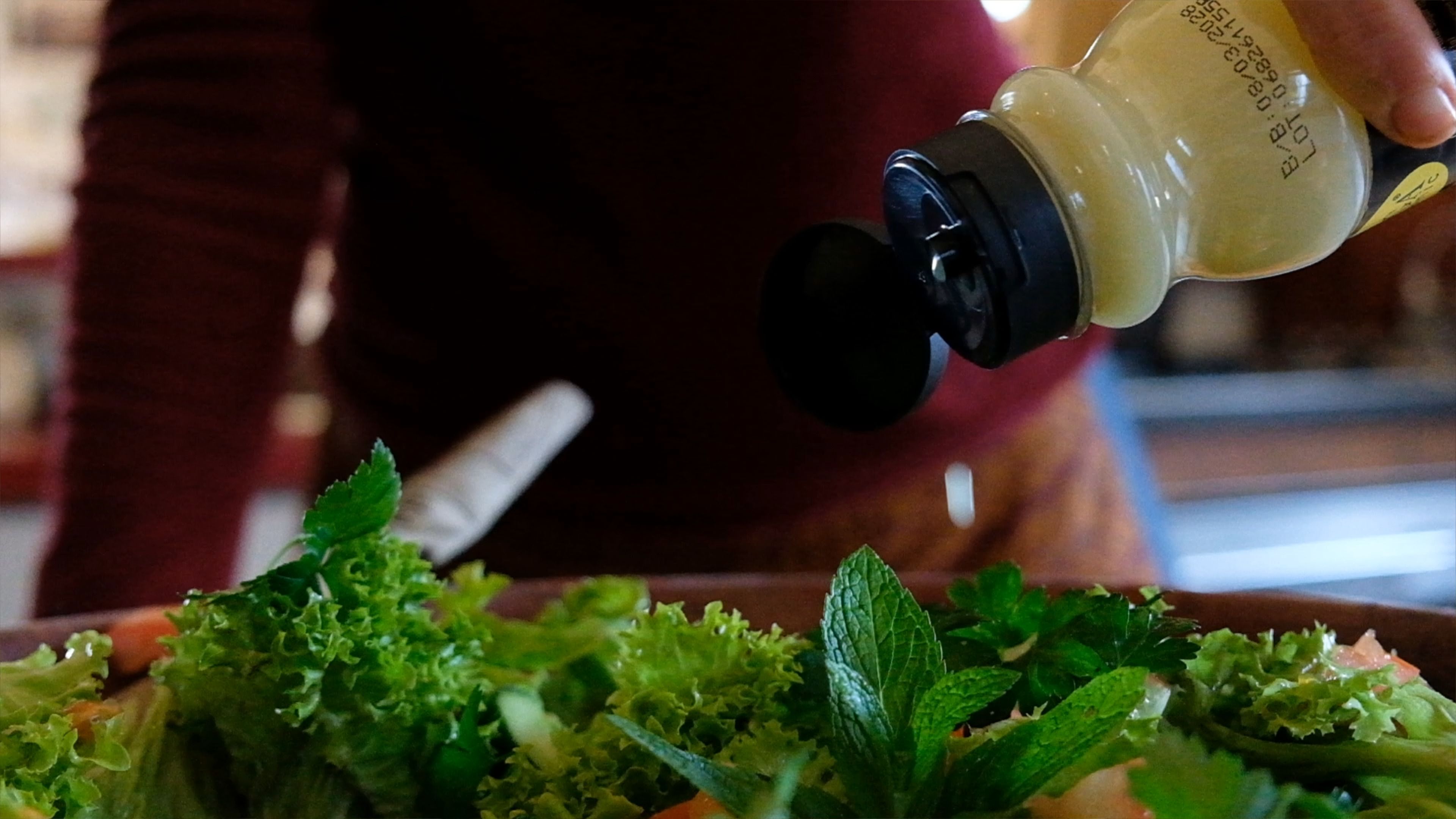Lemon juice being squeezed from a bottle over a fresh herb salad