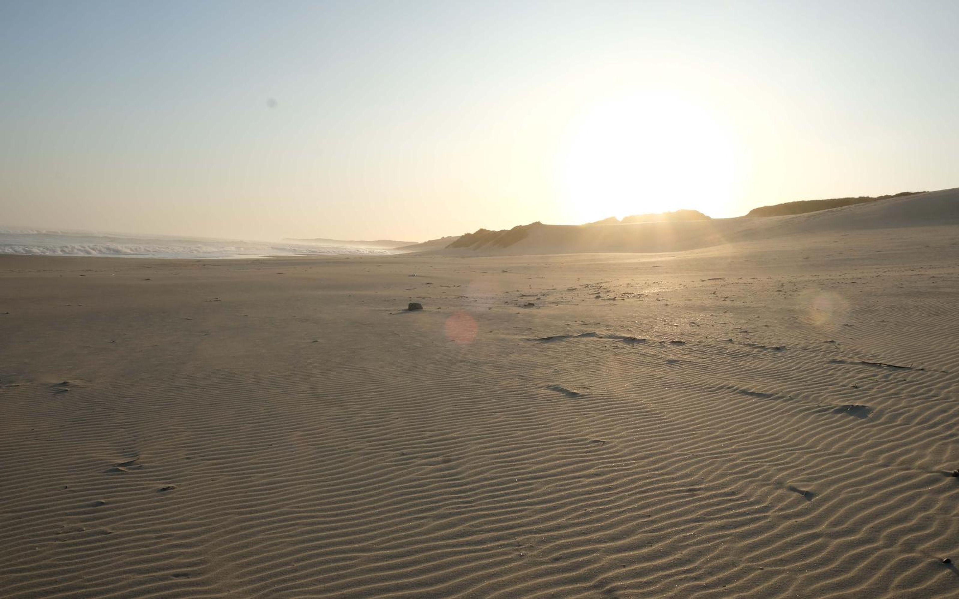 Sun low over a dune ridge above a wide beach floor of fine ripples