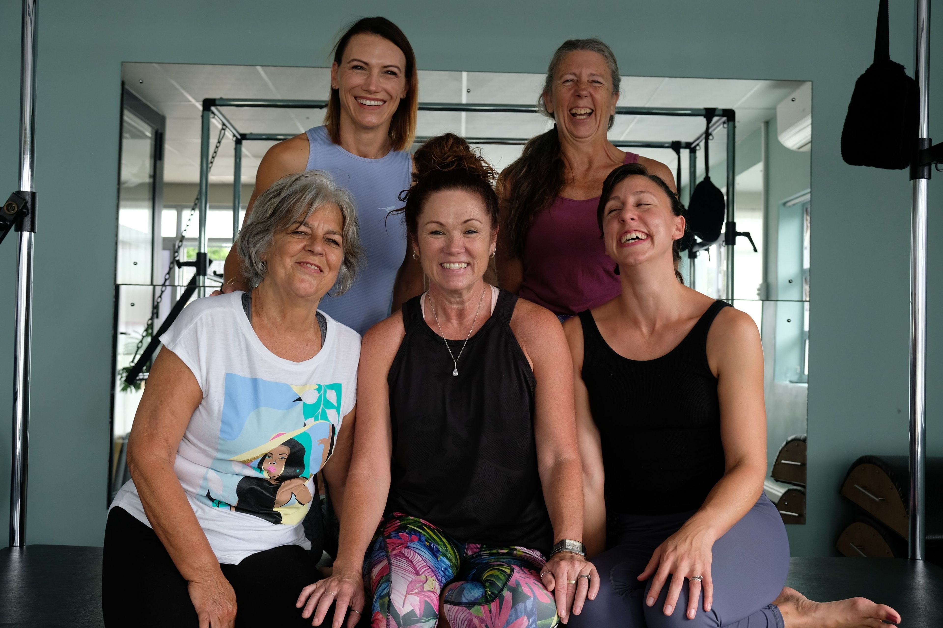 Five instructors laughing together, three seated in front and two standing behind