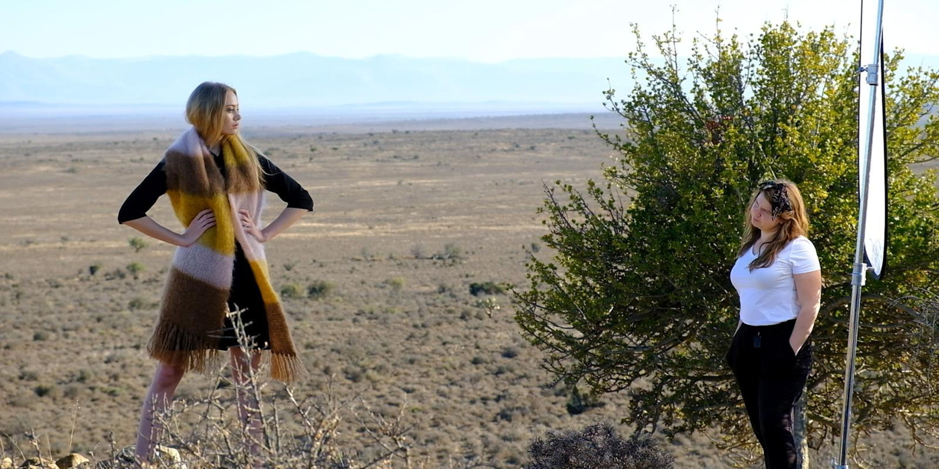 Model in a mustard mohair scarf on the veld with a crew member nearby