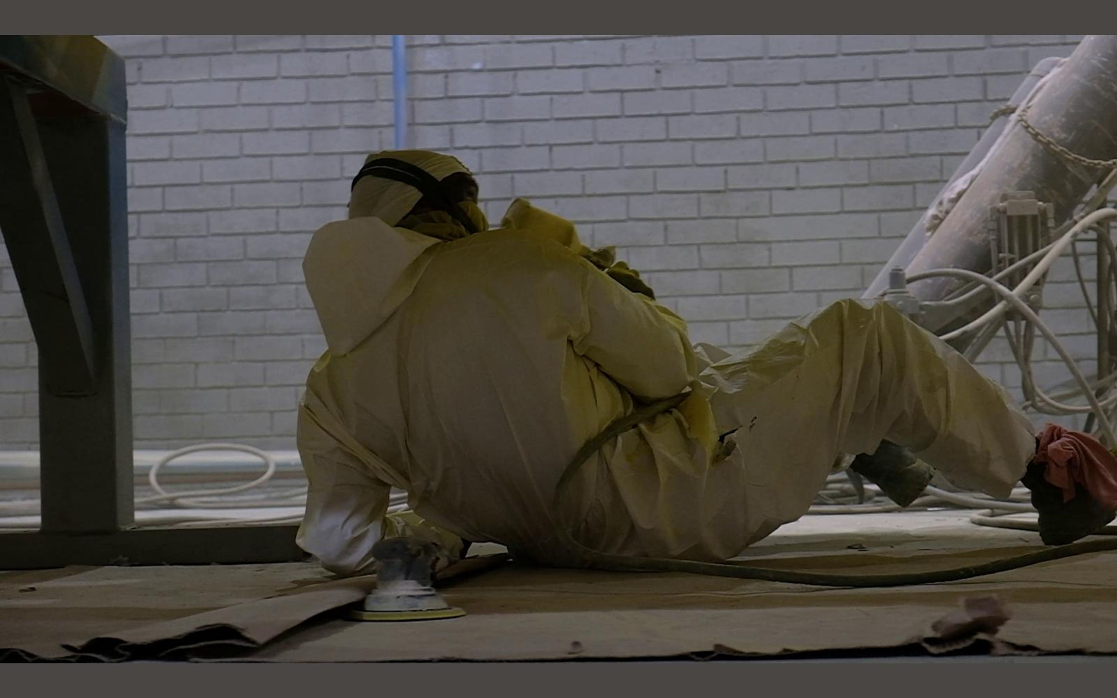 Painter lying on the floor spraying the underside of a steel frame