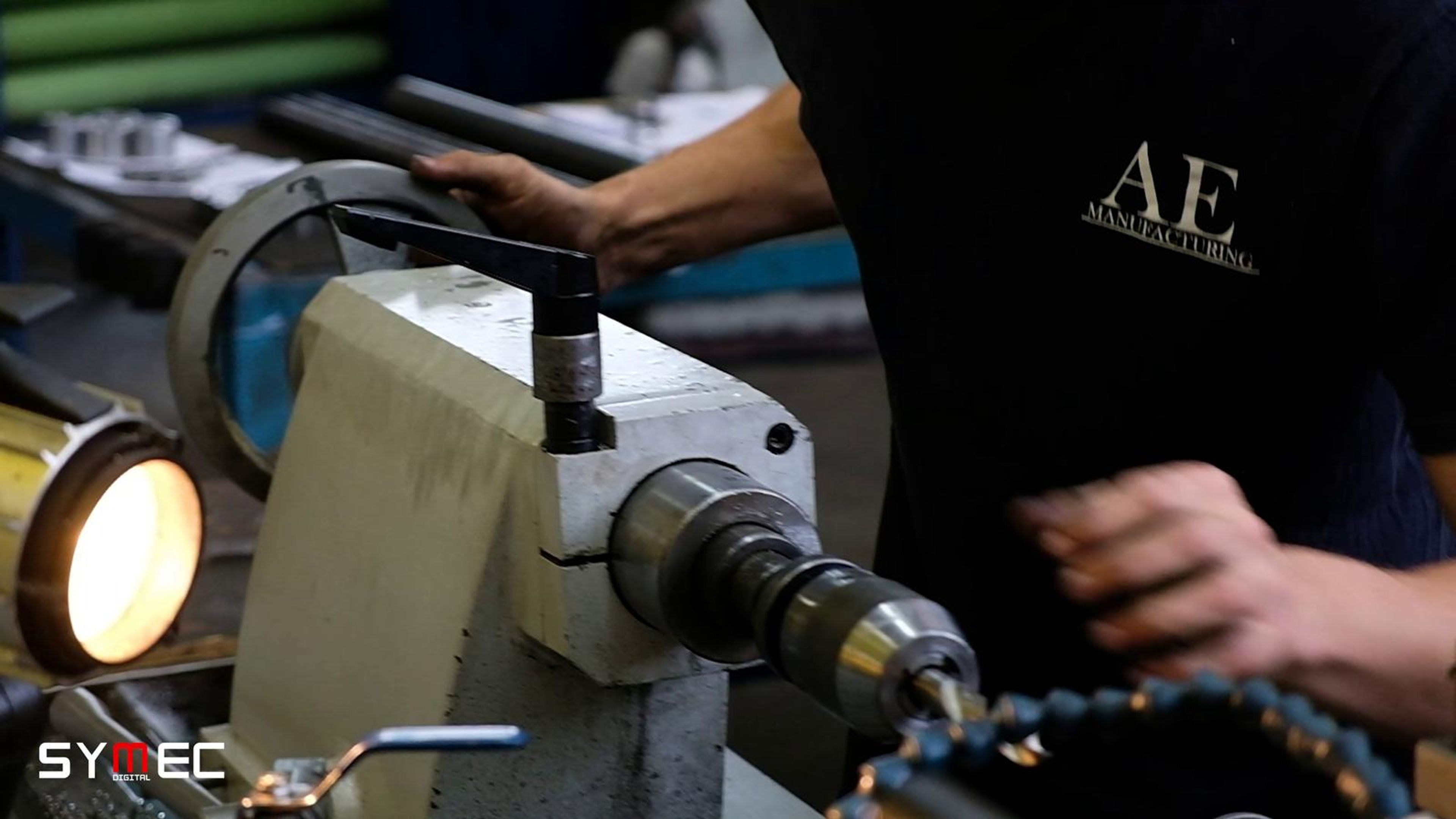 Machinist in an AE shirt at a lathe with a work light