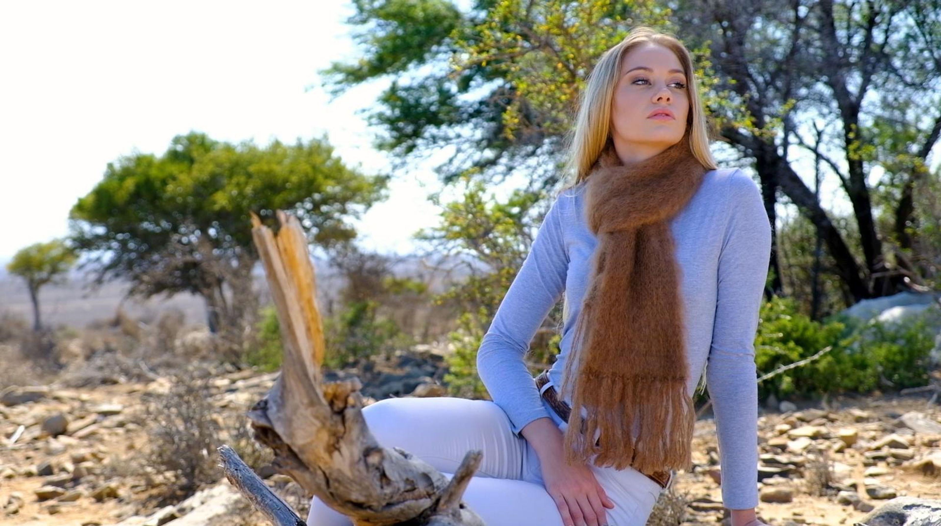 Model seated on driftwood in a brown mohair scarf