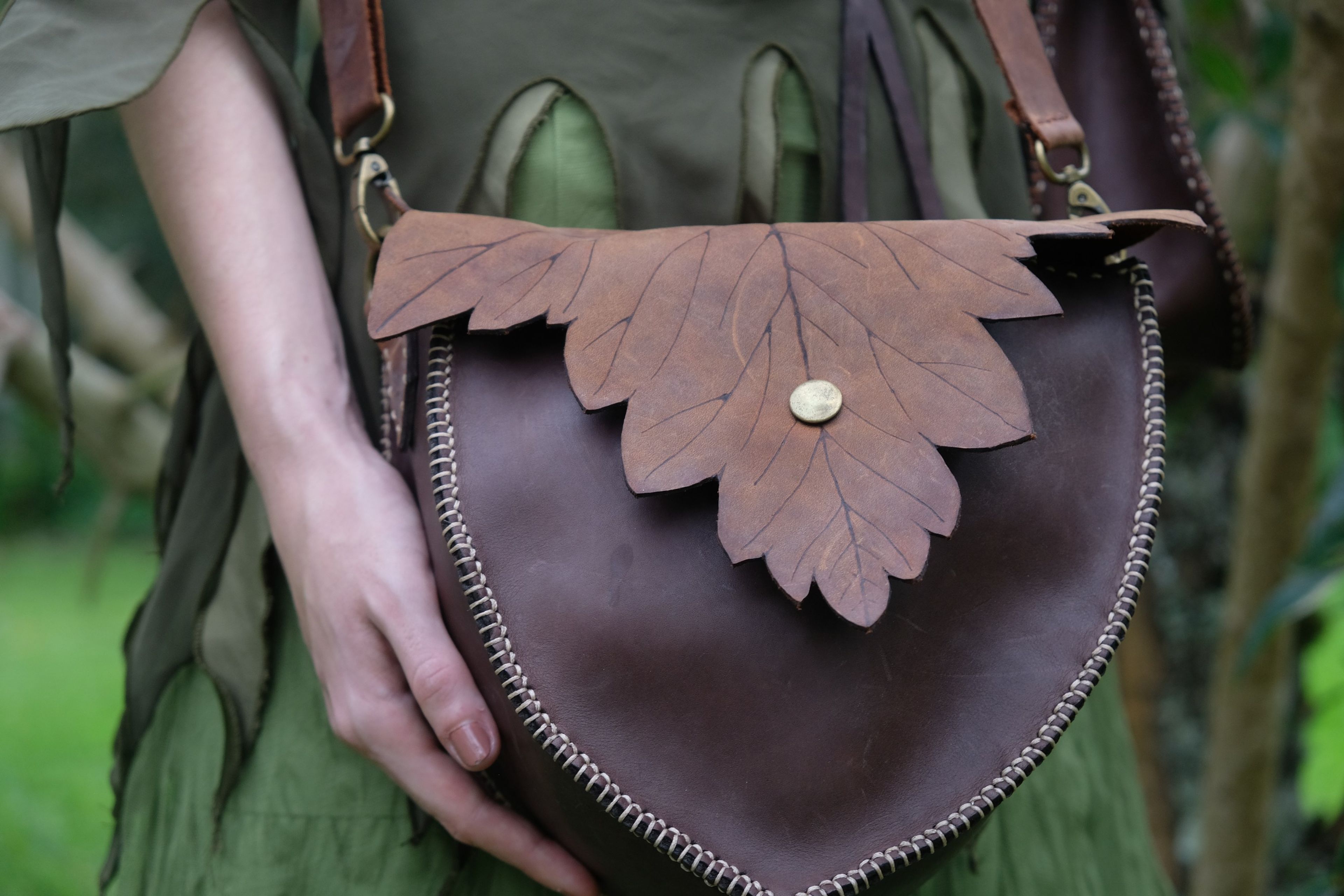 Brown and tan leather bag with an oak-leaf flap held at the hip