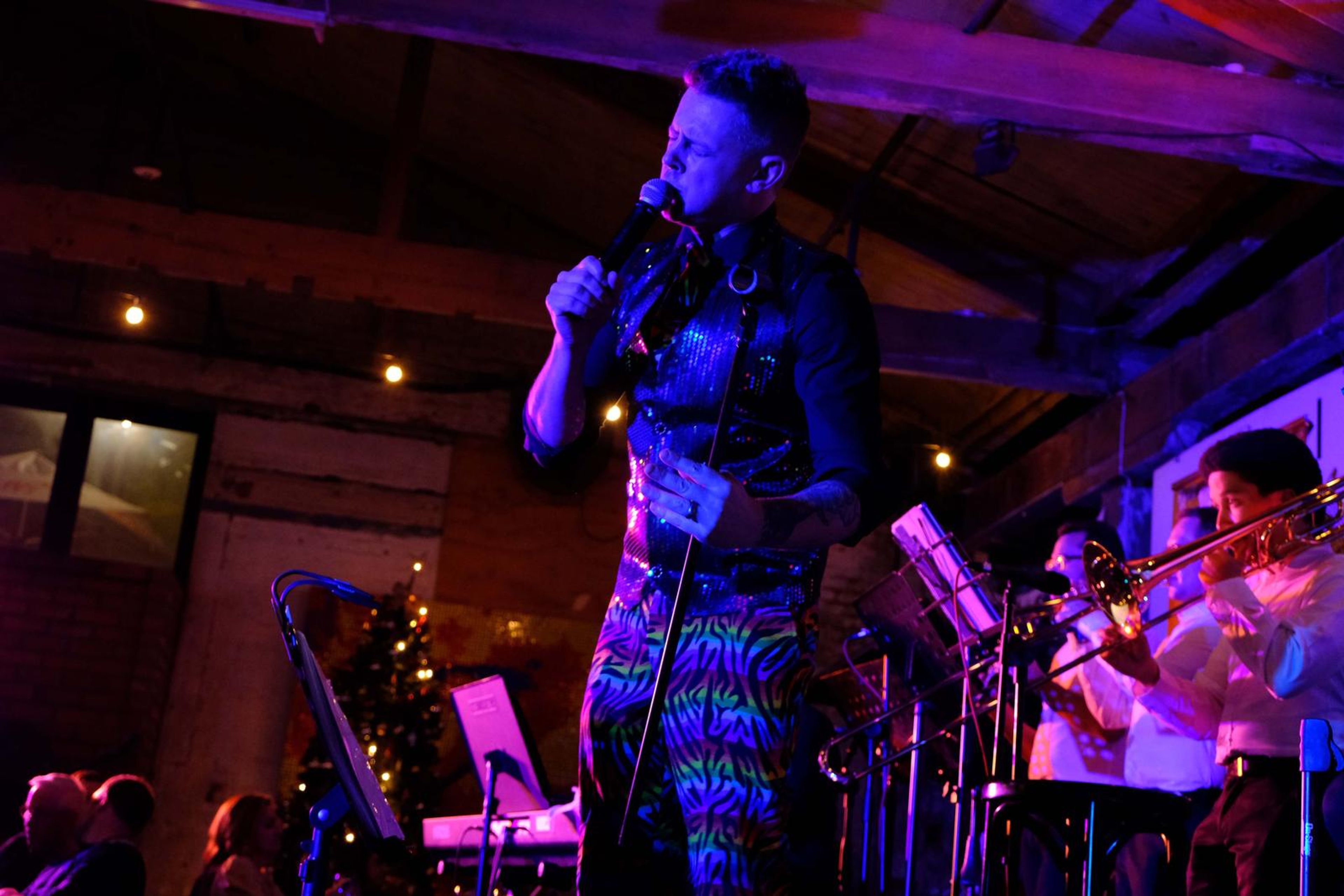 Singer on stage in rainbow trousers with the trombone player behind