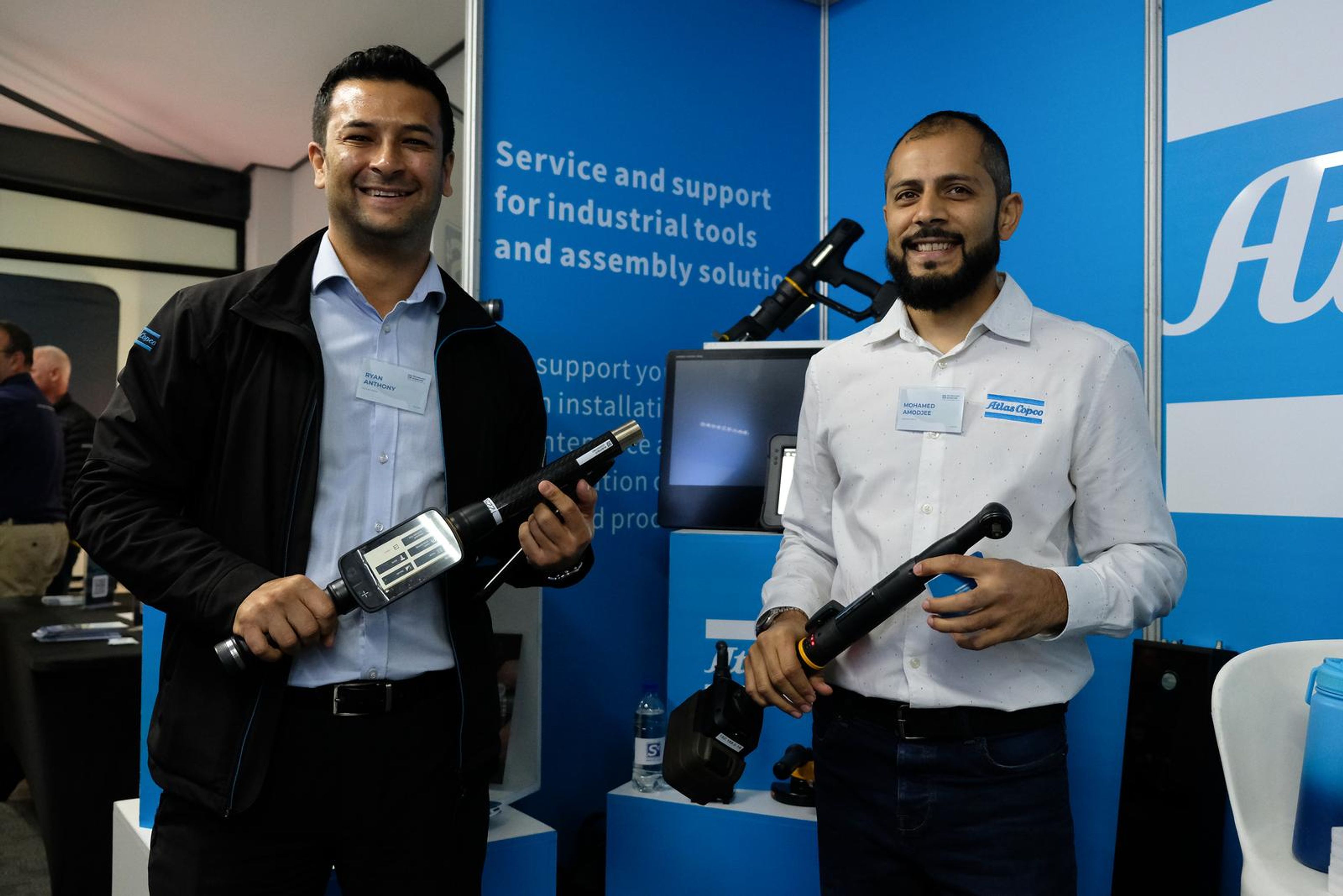 Two Atlas Copco team members at their stand with a handheld tool